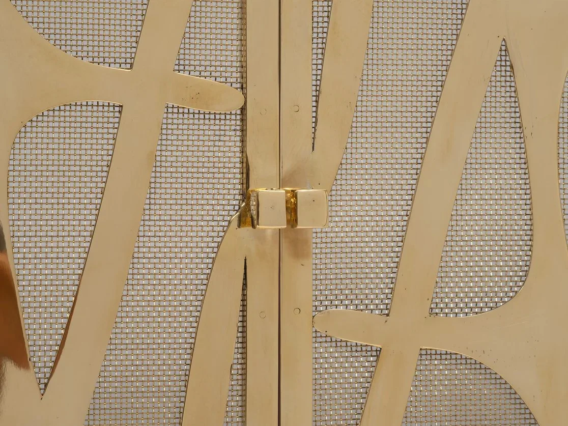 Close-up detail of the cast bronze overlay and mesh construction on the Volta Fire Screen