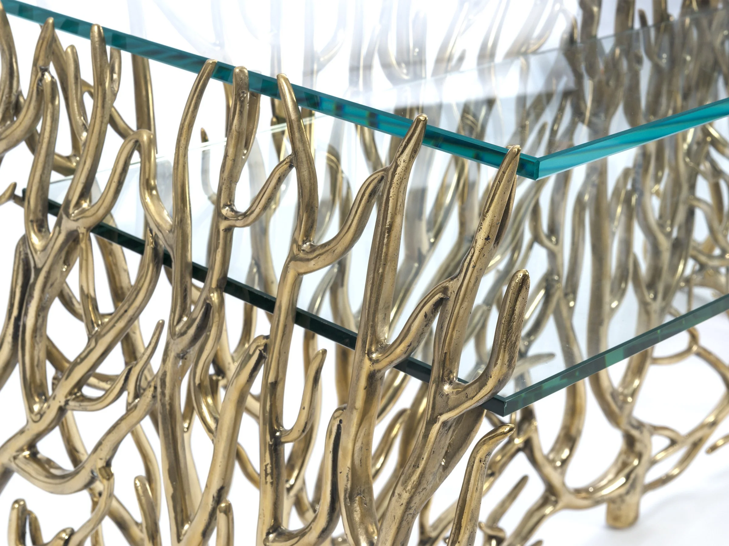 Detail view of the Artis Desk's polished bronze frame with coral-inspired openwork design and glass top