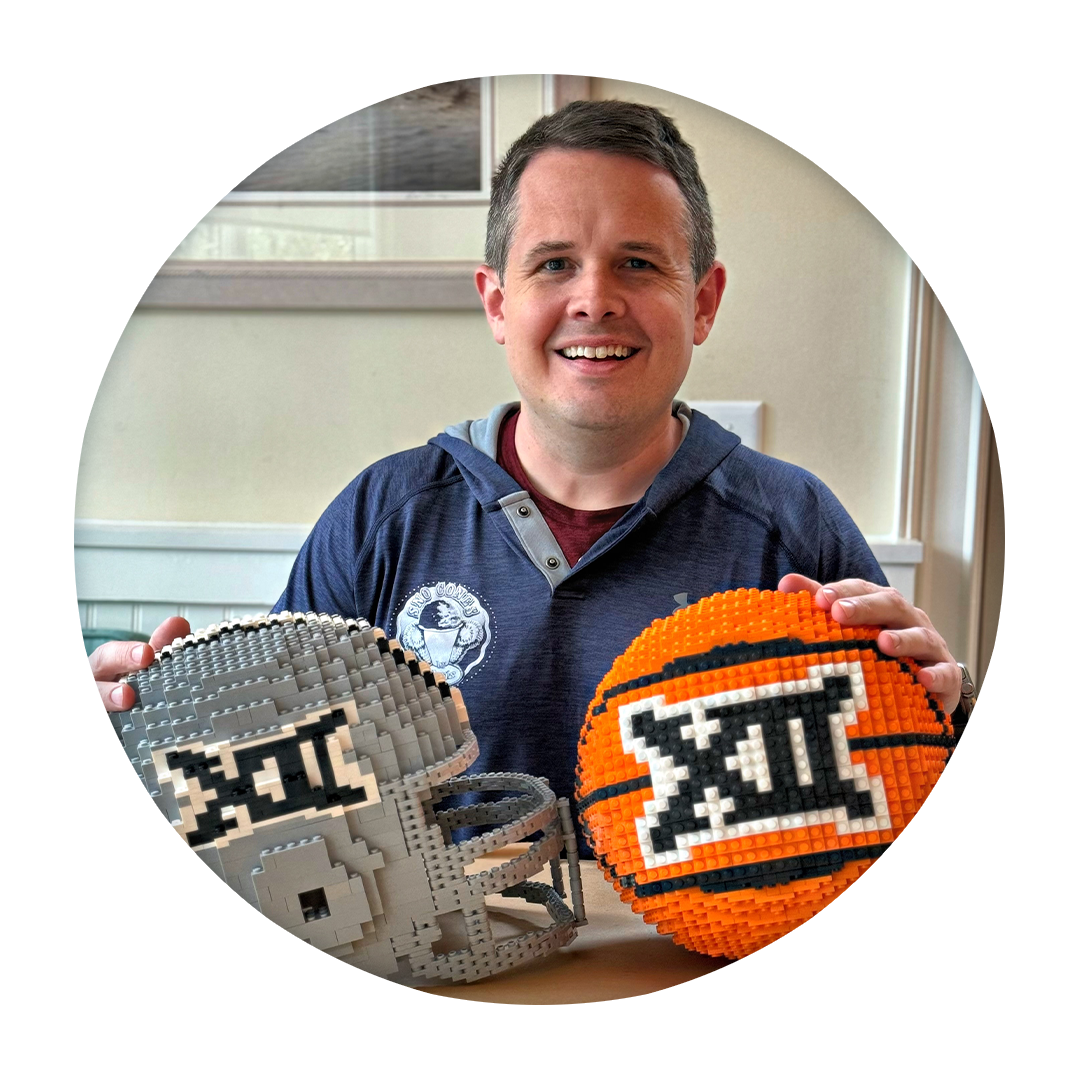 A man smiling and holding a Lego basketball and a Lego football helmet.