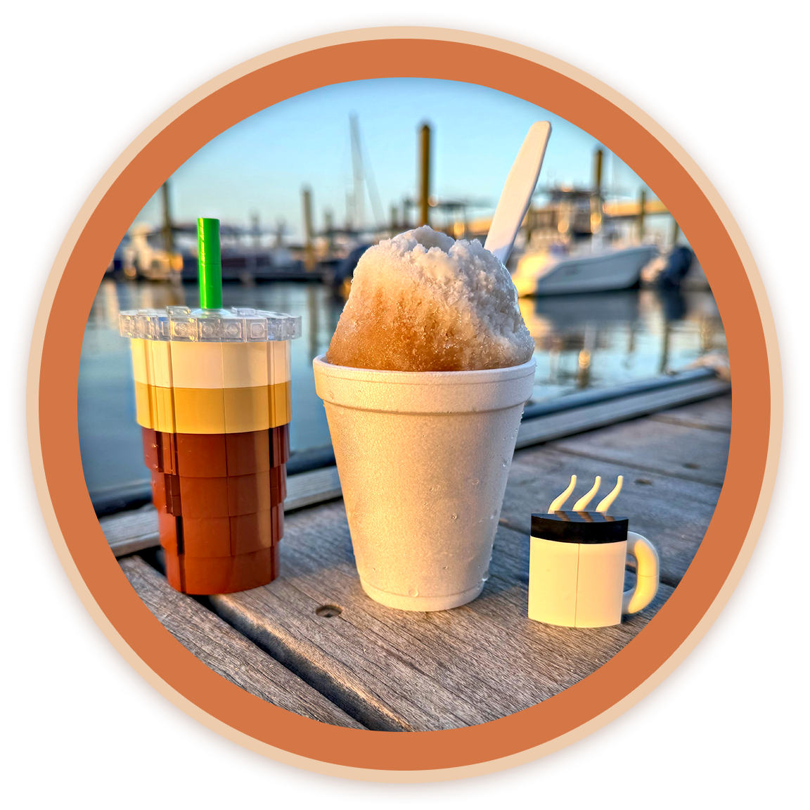 A Lego drink, a snow cone, and a Lego coffee mug with steam, set on a wooden dock near boats and water in the background.