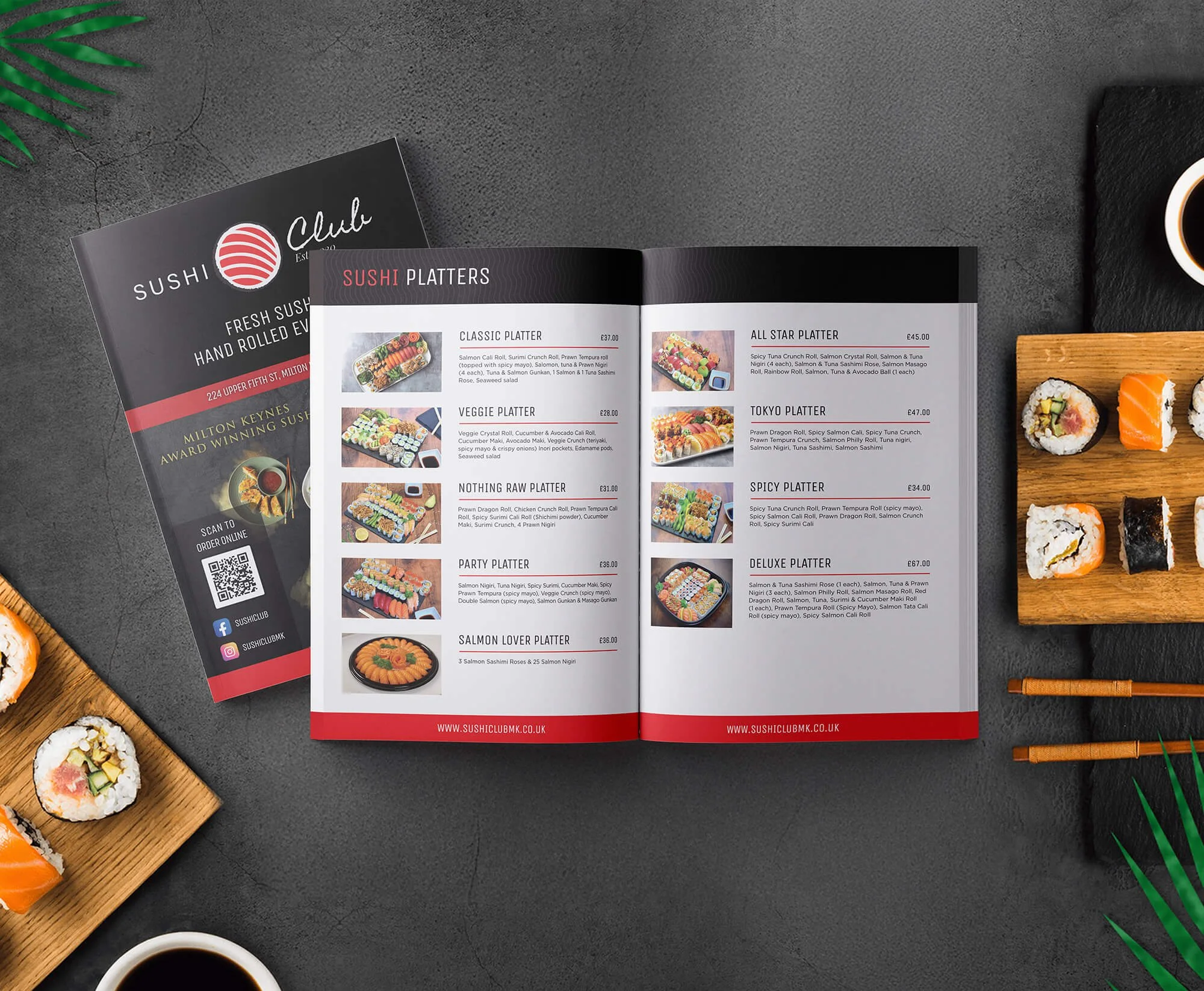 Open sushi menu with various sushi platter options and prices, placed on a dark table with some sushi rolls, soy sauce, chopsticks, and a green plant in the background.