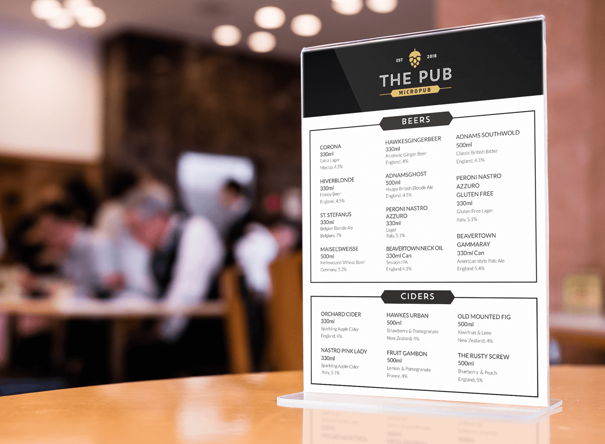 Menu in a restaurant or pub with beer and cider options, placed on a table, with blurred patrons in the background.