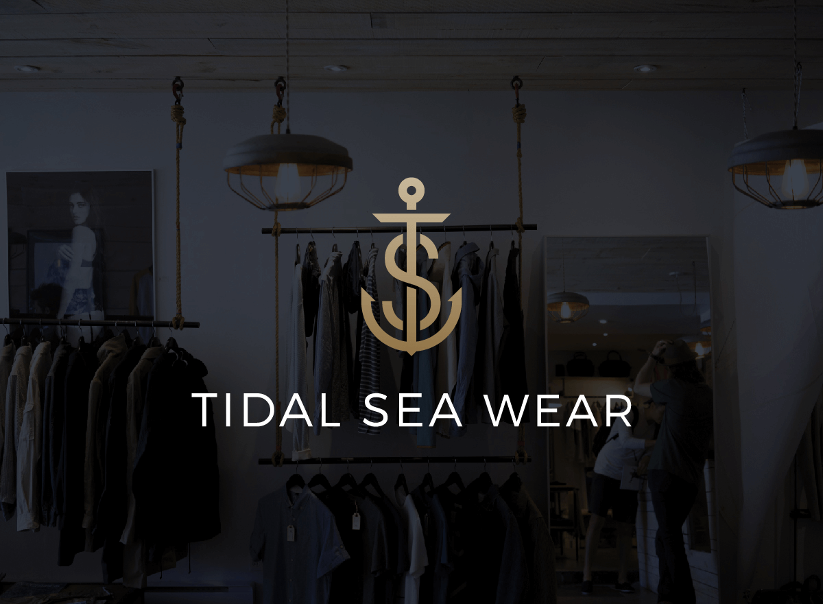 Interior of a clothing store with racks of clothes, a mirror, and hanging light fixtures, featuring a logo with an anchor and the text "Tidal Sea Wear".