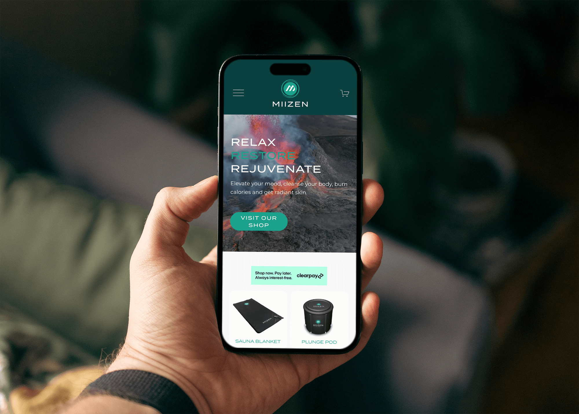 A person holding a smartphone displaying an app called MIIZEN with a website featuring wellness products like sauna blankets and plunge pods.