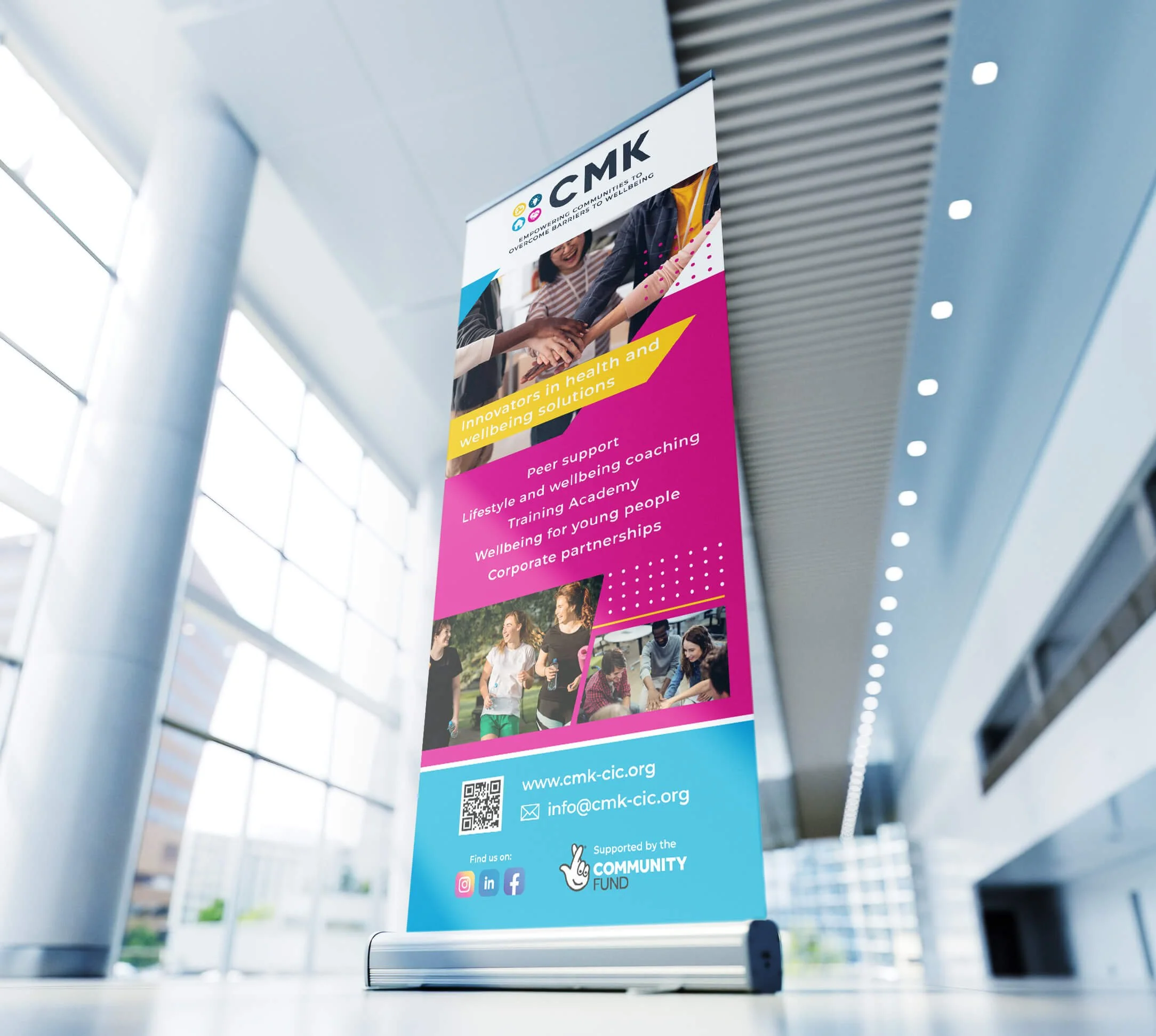 Colorful standing banner inside a modern building promoting health and well-being solutions, featuring images of people exercising and socializing, with contact information and social media icons at the bottom.