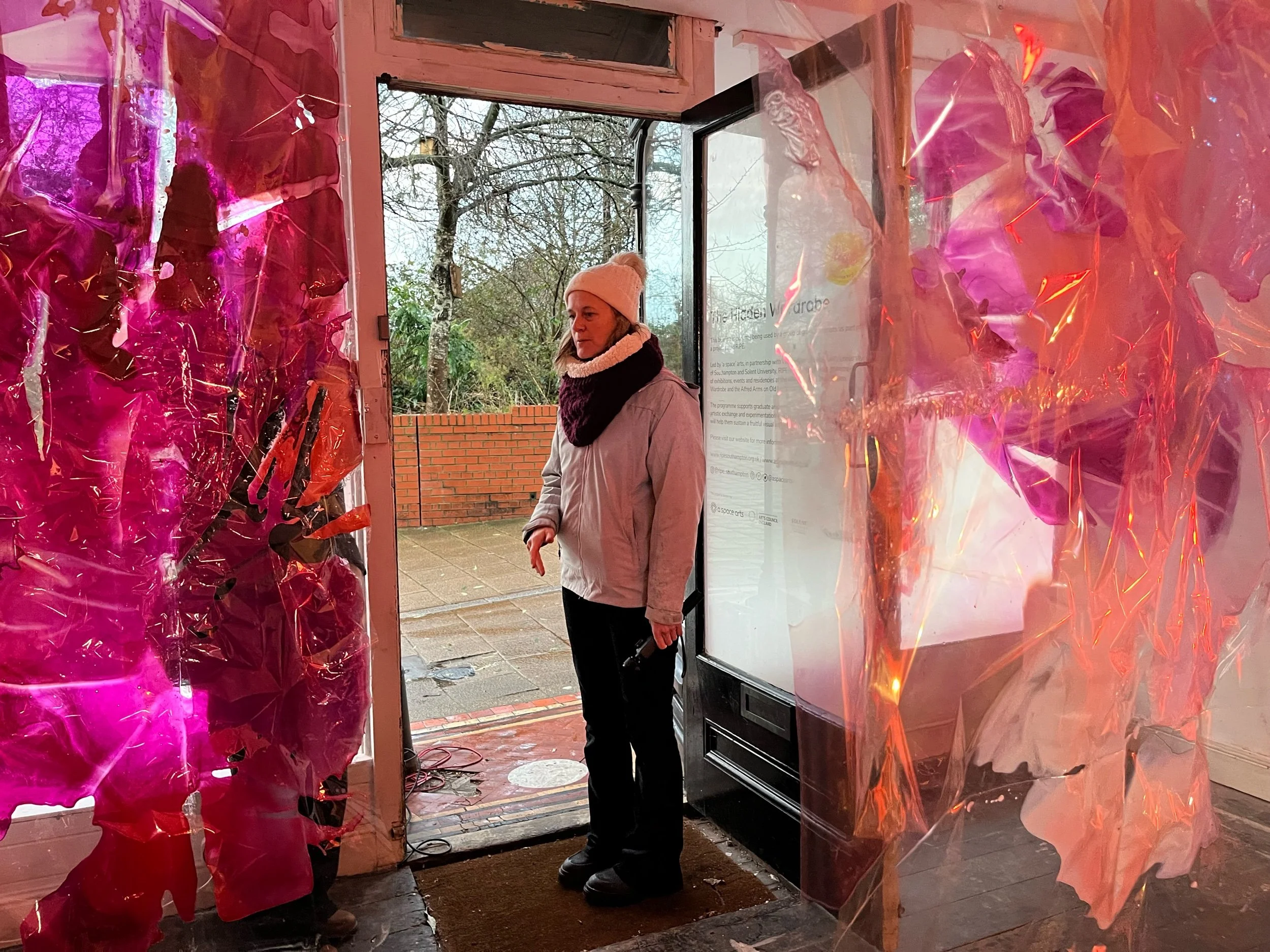 A woman standing inside a building near the entrance, outside on the sidewalk, with clear plastic and pink lighting decorations around the doorway.