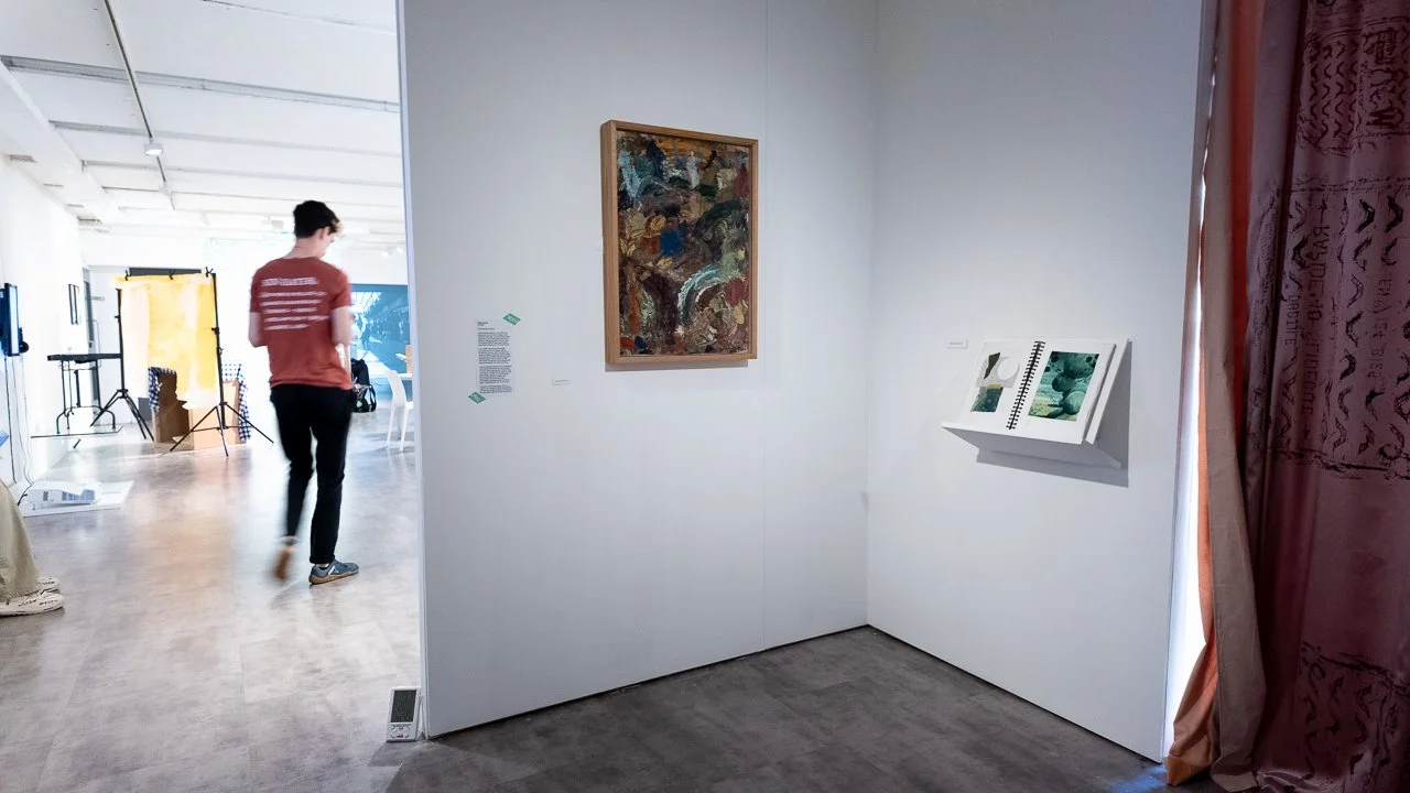 An art gallery with abstract paintings on white walls, a person walking through, and a curtain on the right side.