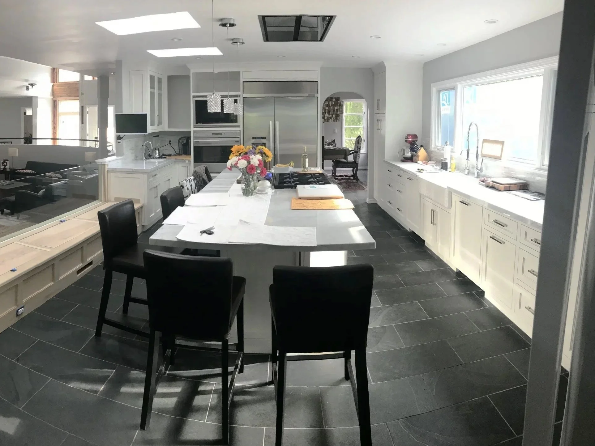 Modern kitchen with white cabinets, black chairs around a central island, and a large window providing natural light.