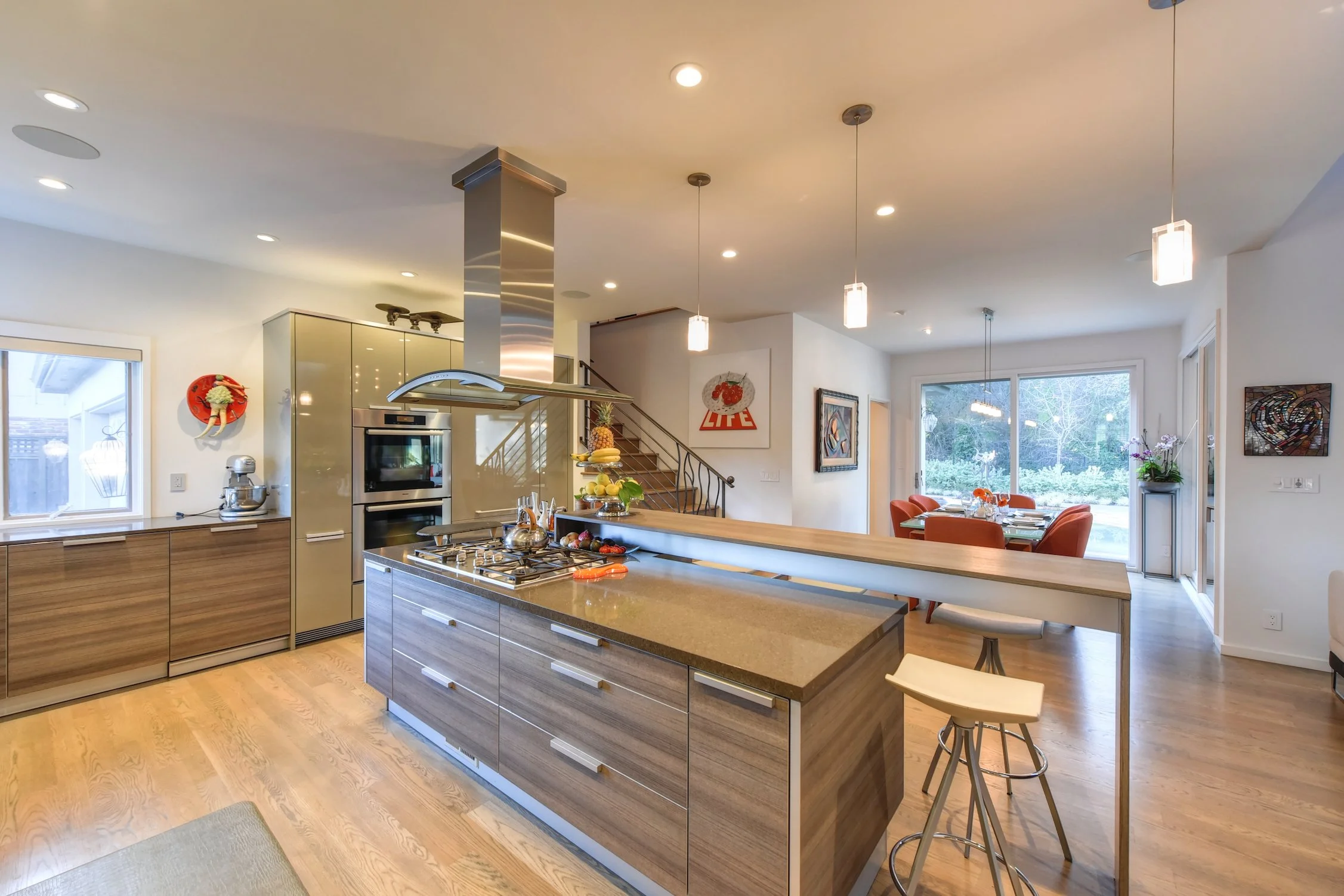 Modern open-concept kitchen with a kitchen island, wooden cabinets, stainless steel appliances, and a dining area with orange chairs.