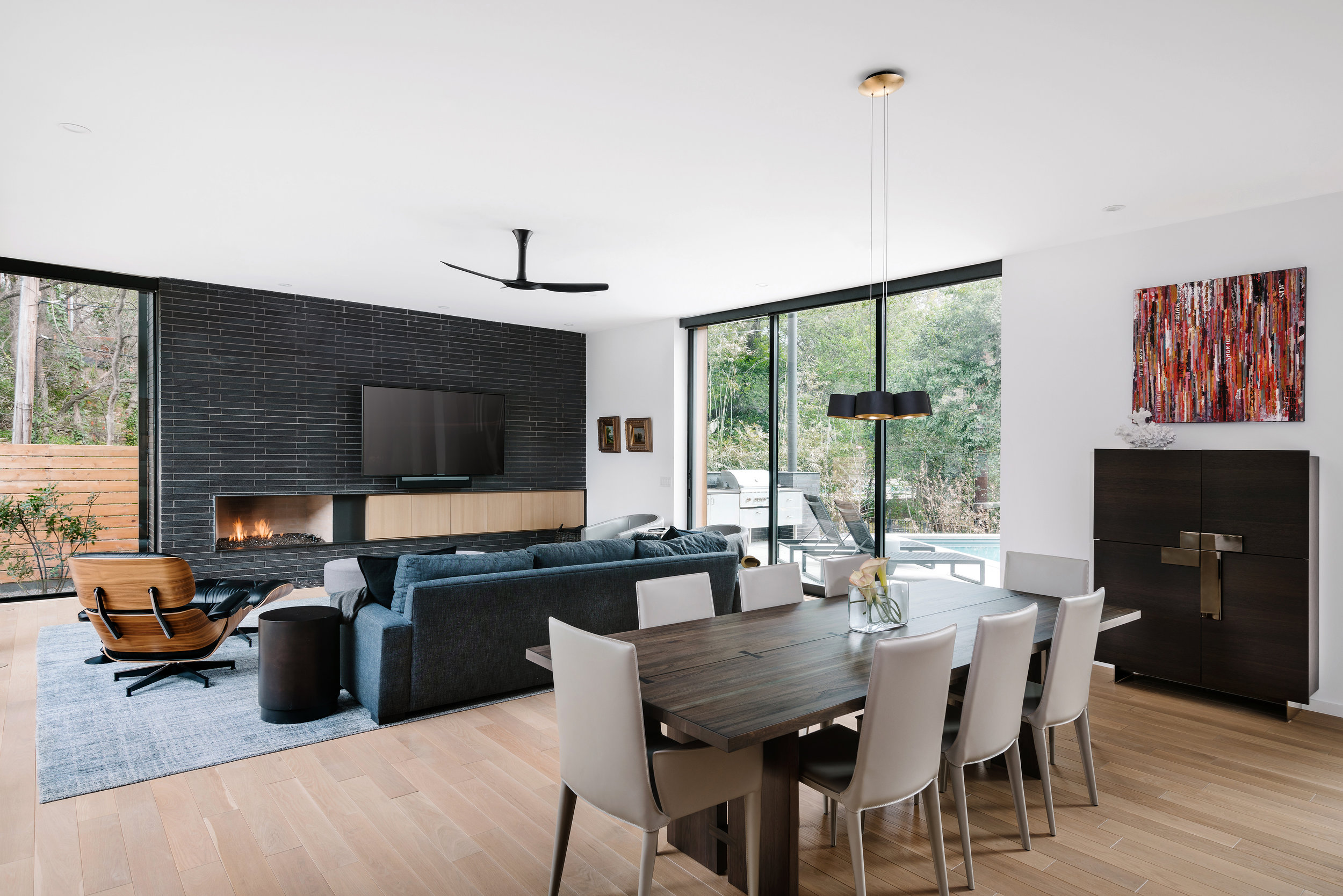 Modern open-concept living and dining area in the Pecos Residence with large windows, a fireplace, a dark blue sofa, and contemporary furniture.