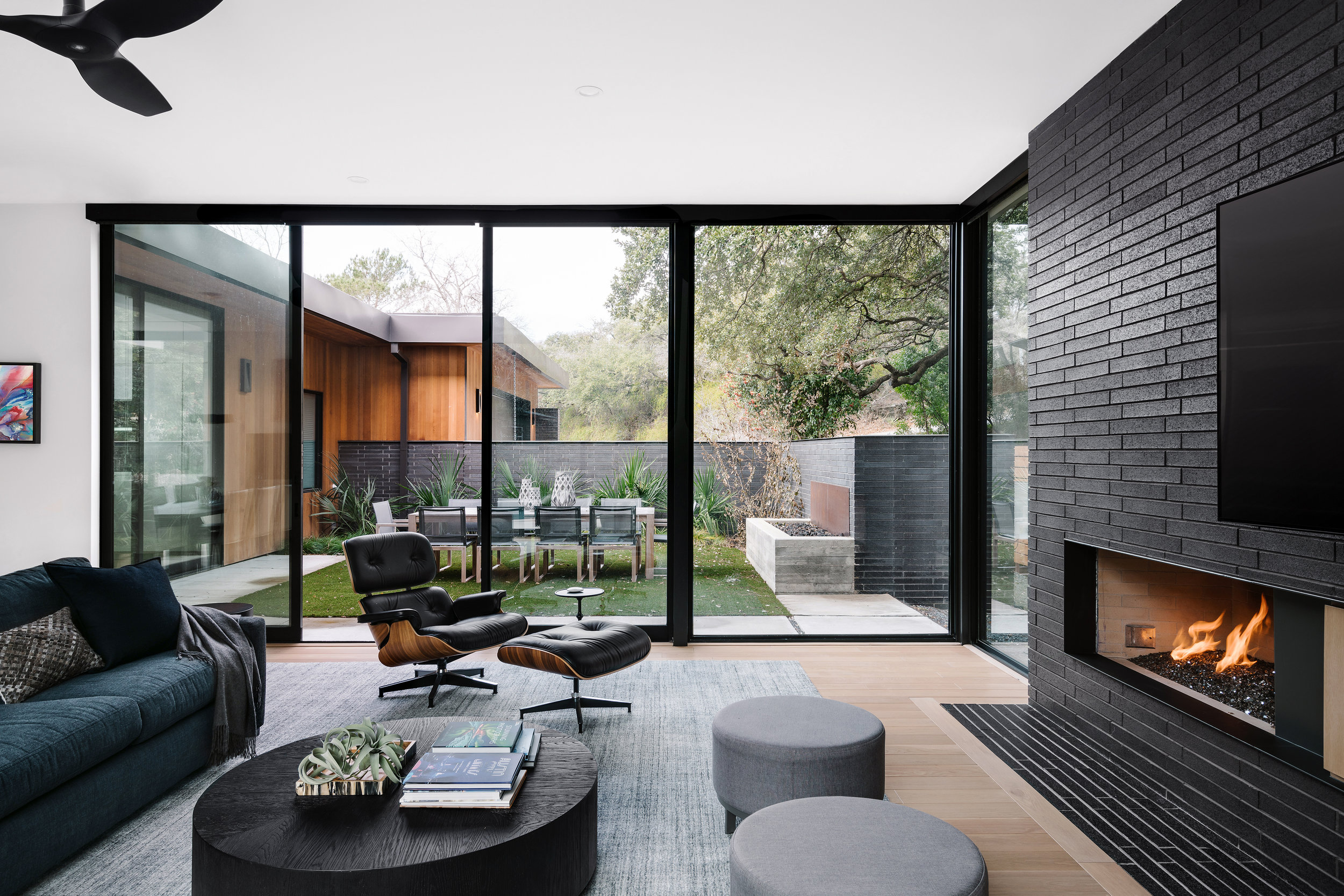 Modern living room in the Pecos Residence with black accent wall, fireplace, and large glass doors opening to a patio with outdoor seating.