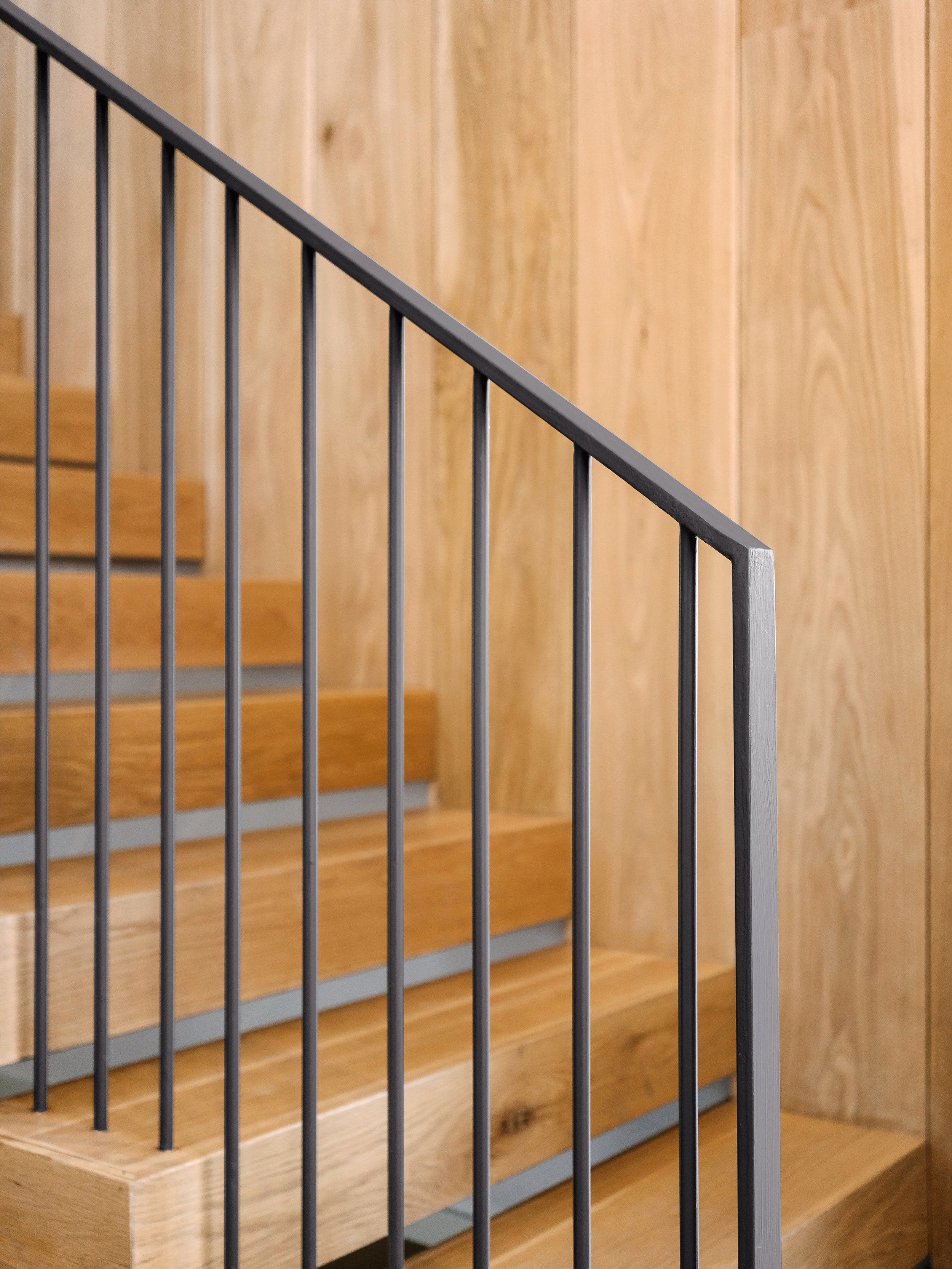 Wooden staircase in the Pecos Residence with black metal railing, set against a wooden paneled wall.