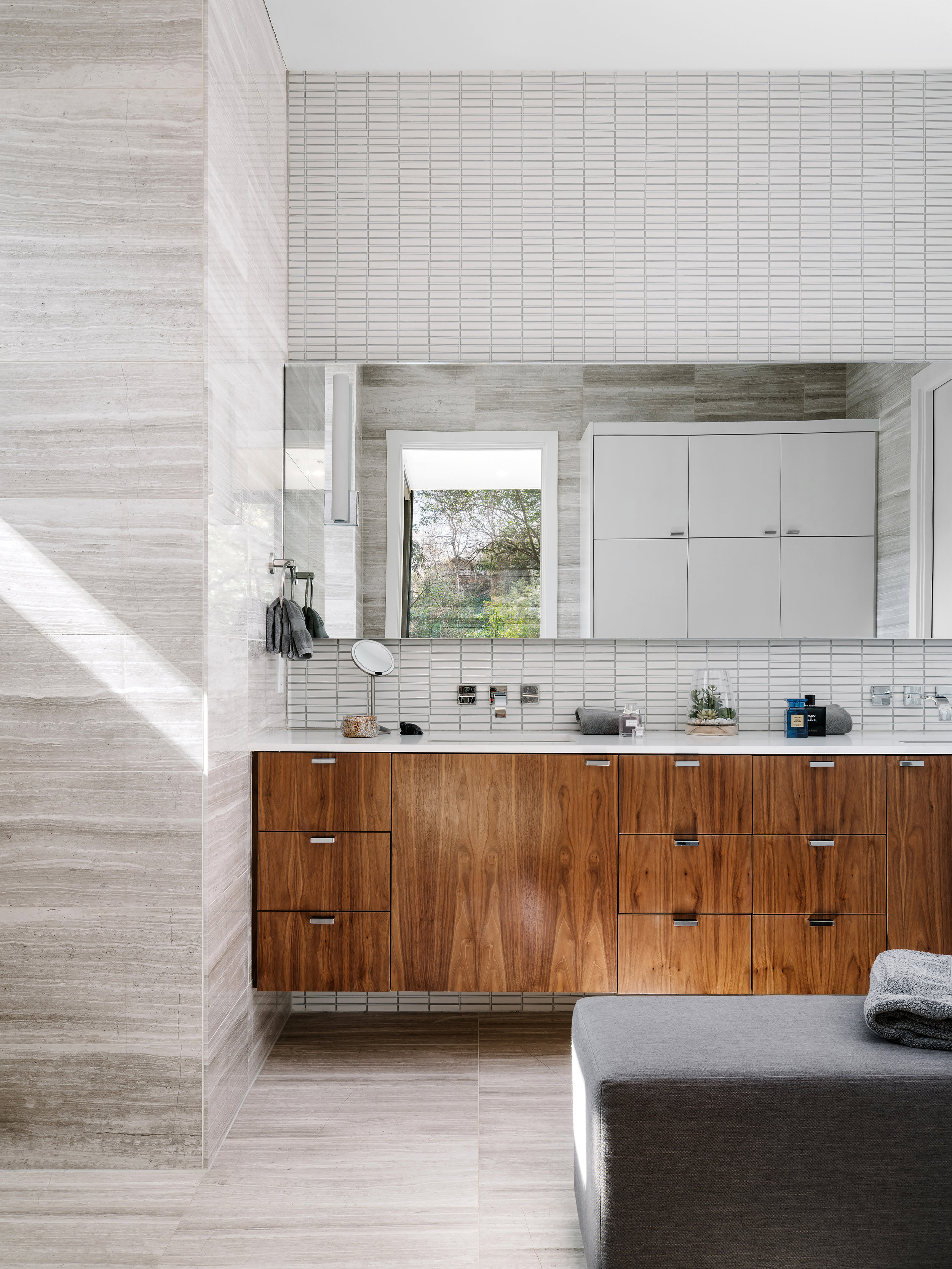 Modern bathroom in the Pecos Residence with wooden cabinets, large mirror, and small window. Light streams in from the right.