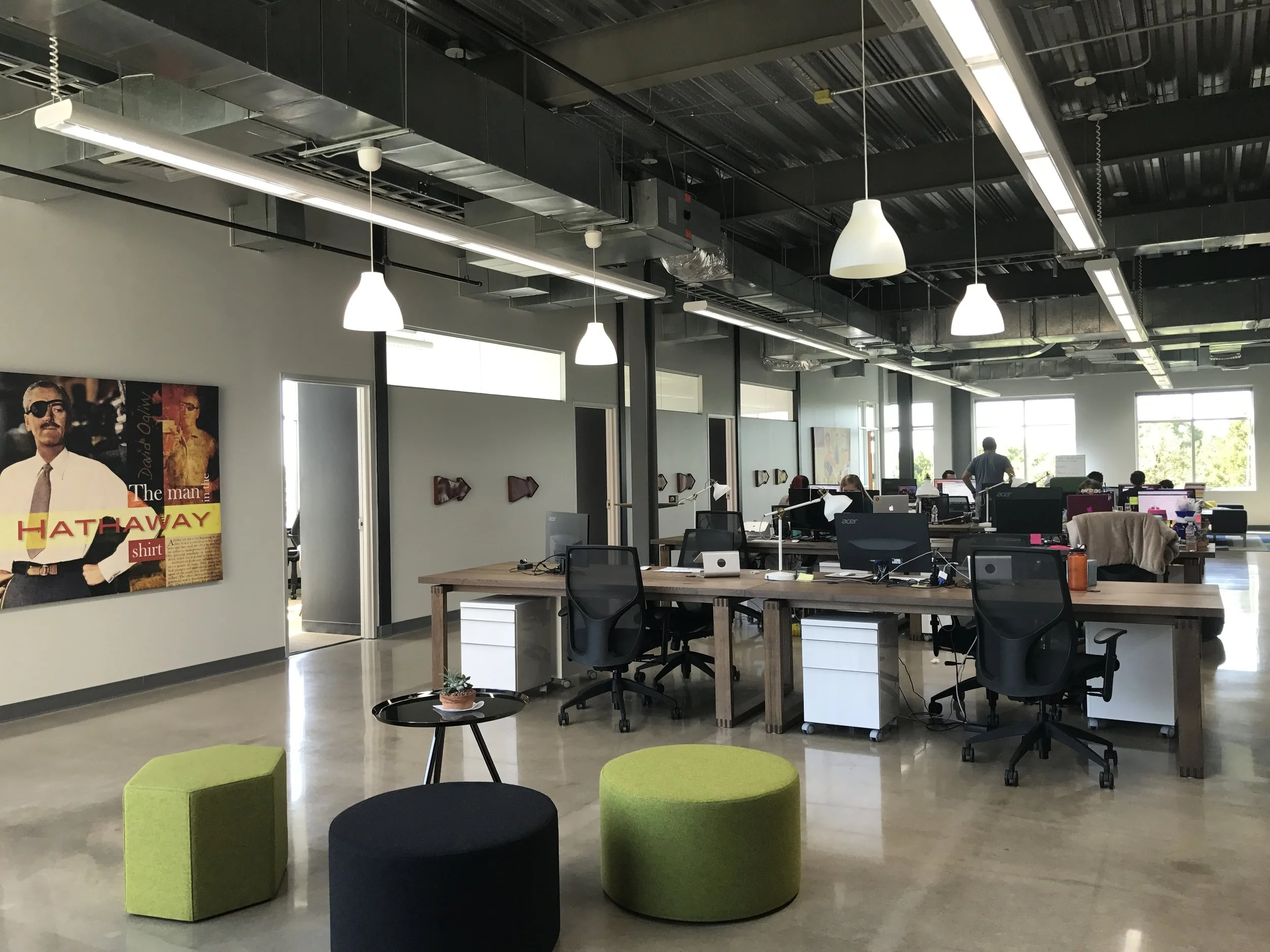  The Digital Marketer office space with desks, chairs, computers, posters and art on the walls, and industrial lighting hanging above. 