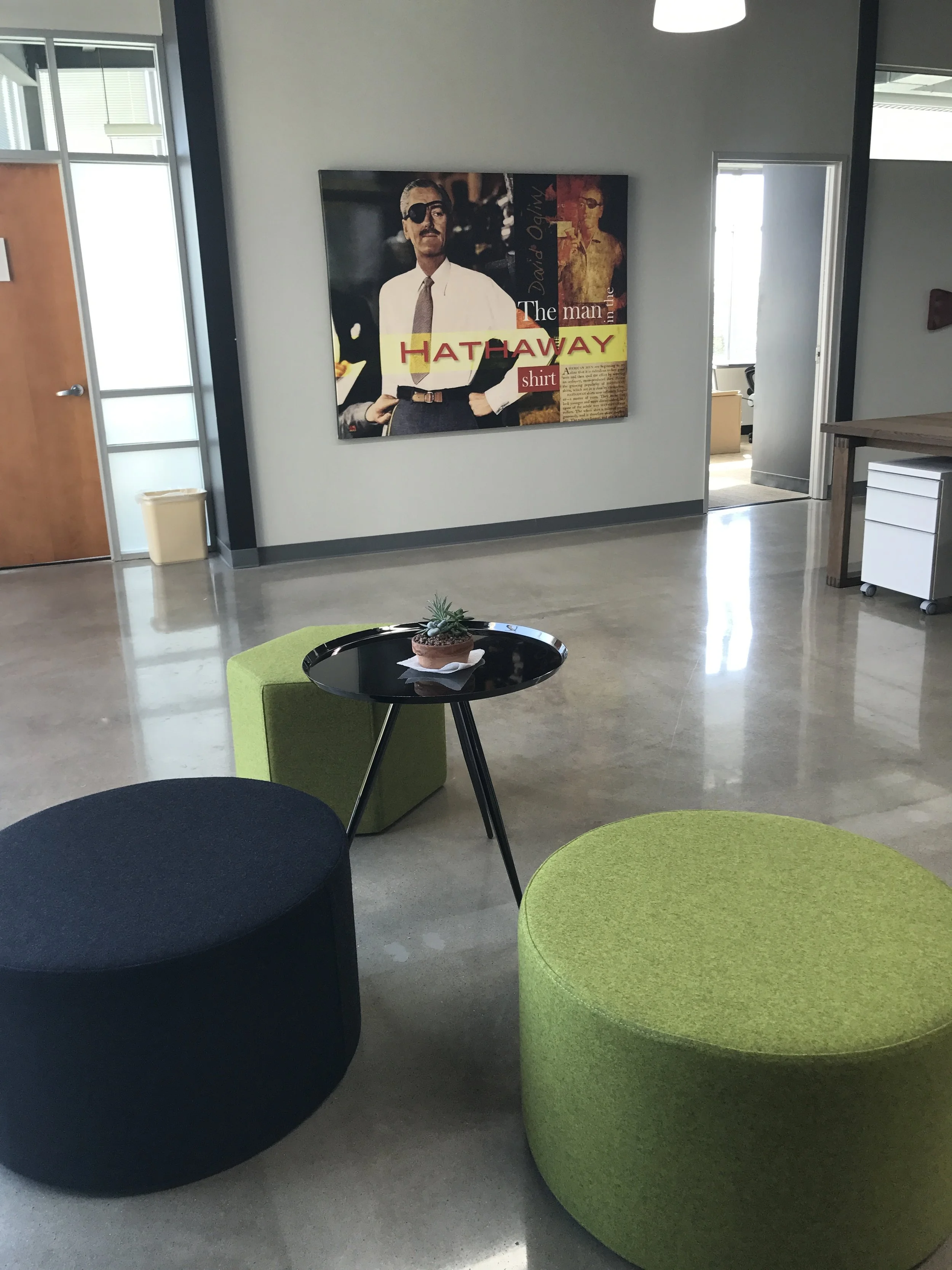  Spacious Digital Marketer office lounge with black and a green ottomans around a small black table, a potted plant, and artwork on a wall. 