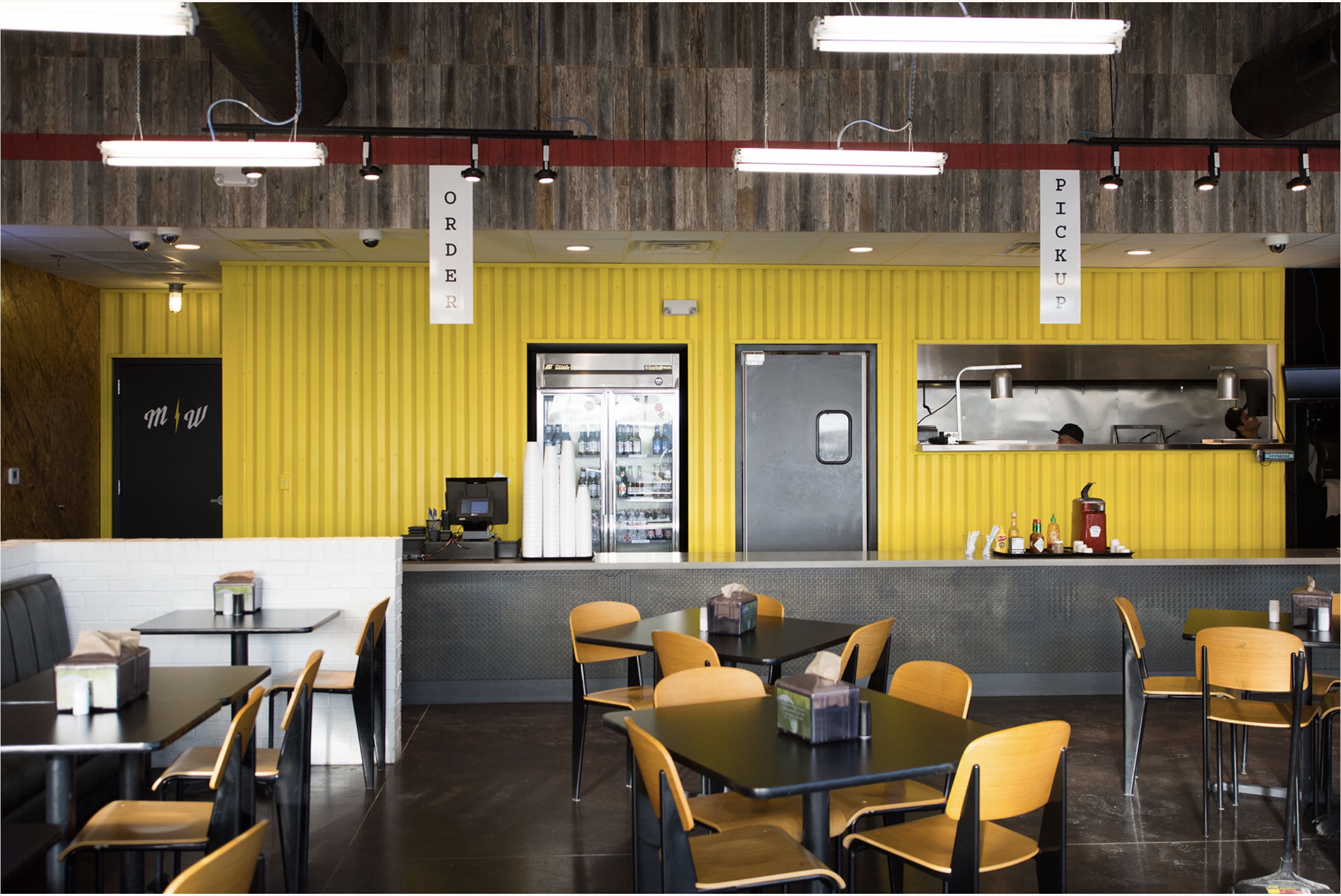 Bright Flash Burger restaurant with yellow walls, industrial decor, a long counter, and tables and chairs set up in the dining area.