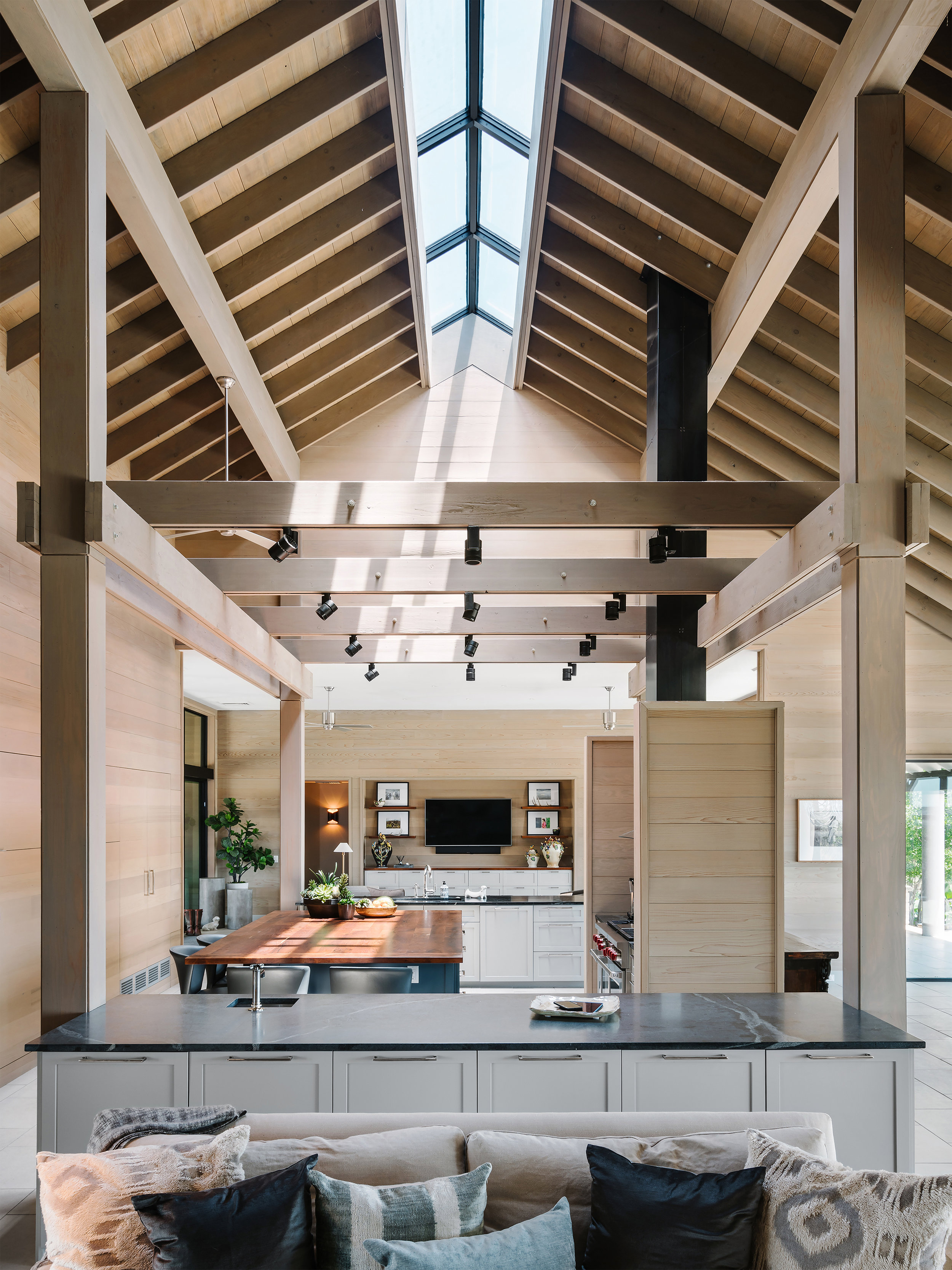 Open-concept living space in a Lampassas ranch home with high wooden ceilings, skylights, modern kitchen, and a cozy sofa in the foreground.
