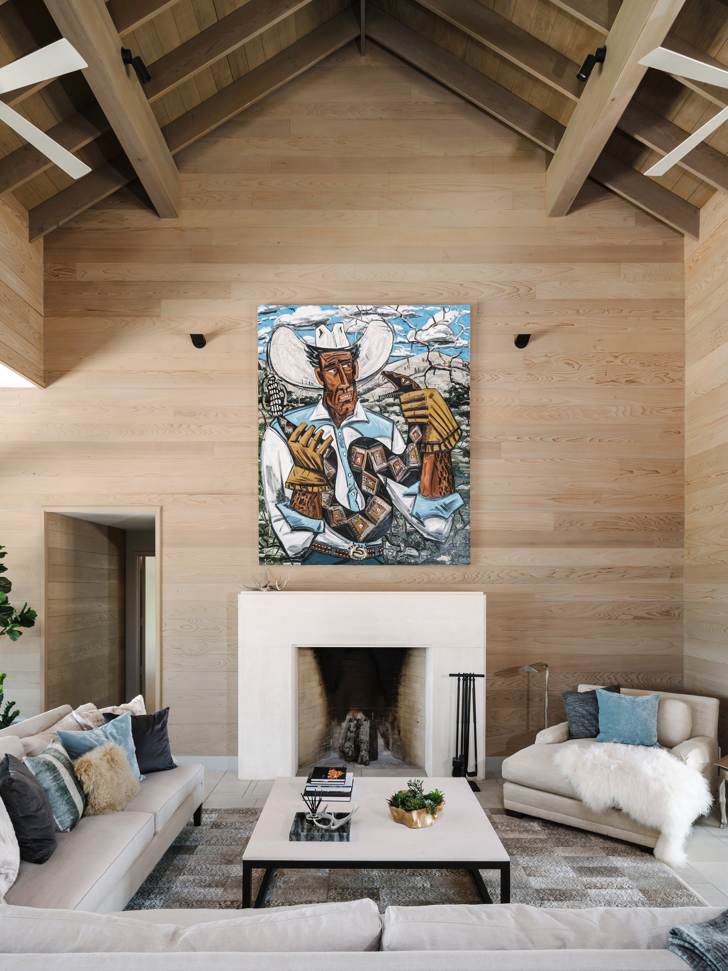 Living room in a Lampassas ranch home with high wooden ceilings, a large colorful painting above a white fireplace, and cozy seating arrangements.