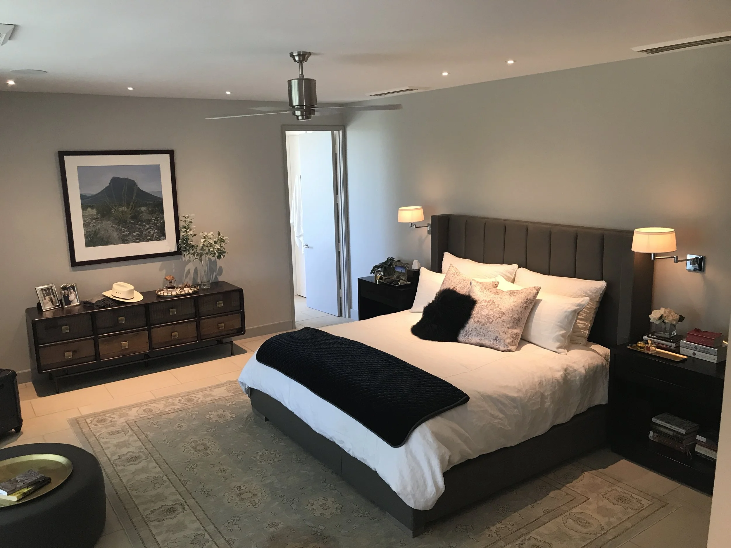  Spacious bedroom in a Lampassas ranch home with a king-size bed, nightstands, lamps, dresser, artwork on the wall, and a ceiling fan. 