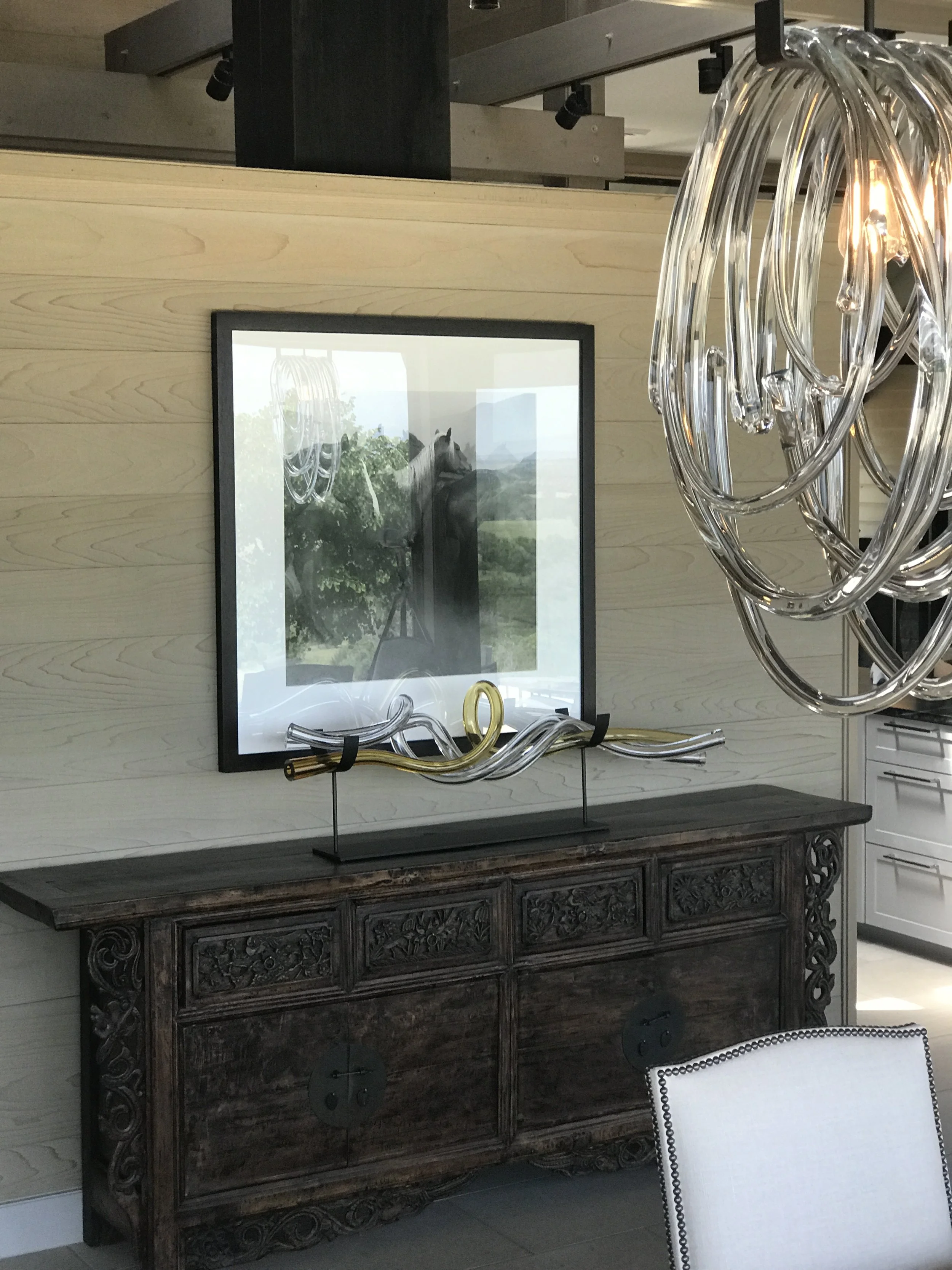  A framed picture, decorative sculpture, and modern lighting adorning a dining room with a rustic dark wood sideboard. 