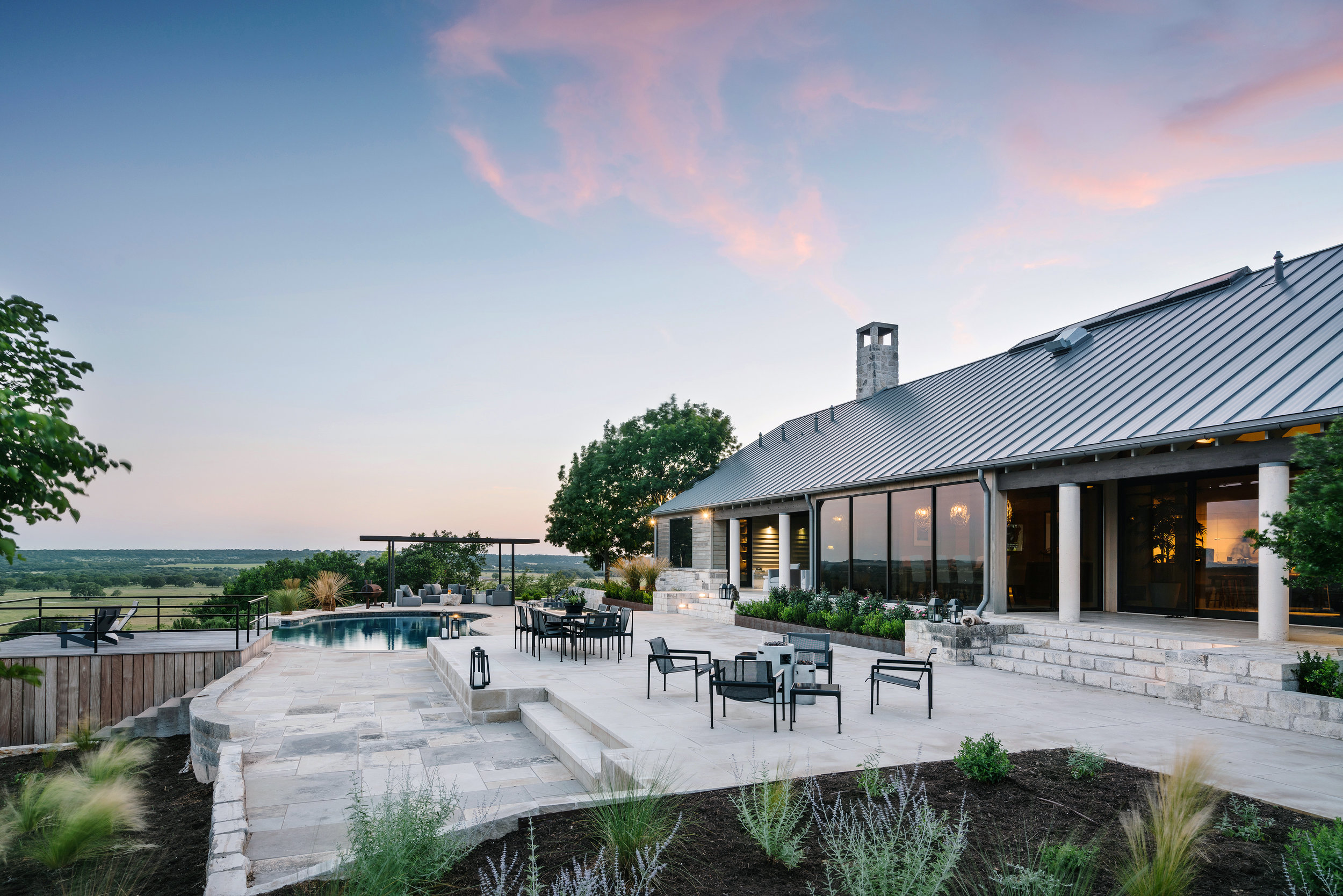 A Lampassas ranch home with large windows, a spacious patio, and a pool, set against a scenic landscape at sunset.