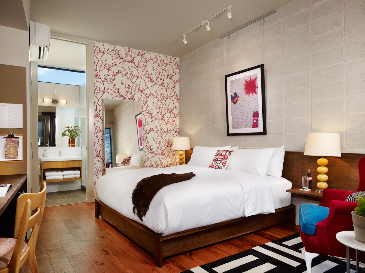 Cozy guest room in the Heywood Hotel with a large bed, nature-themed decor, a vibrant accent chair, and an adjacent modern bathroom.