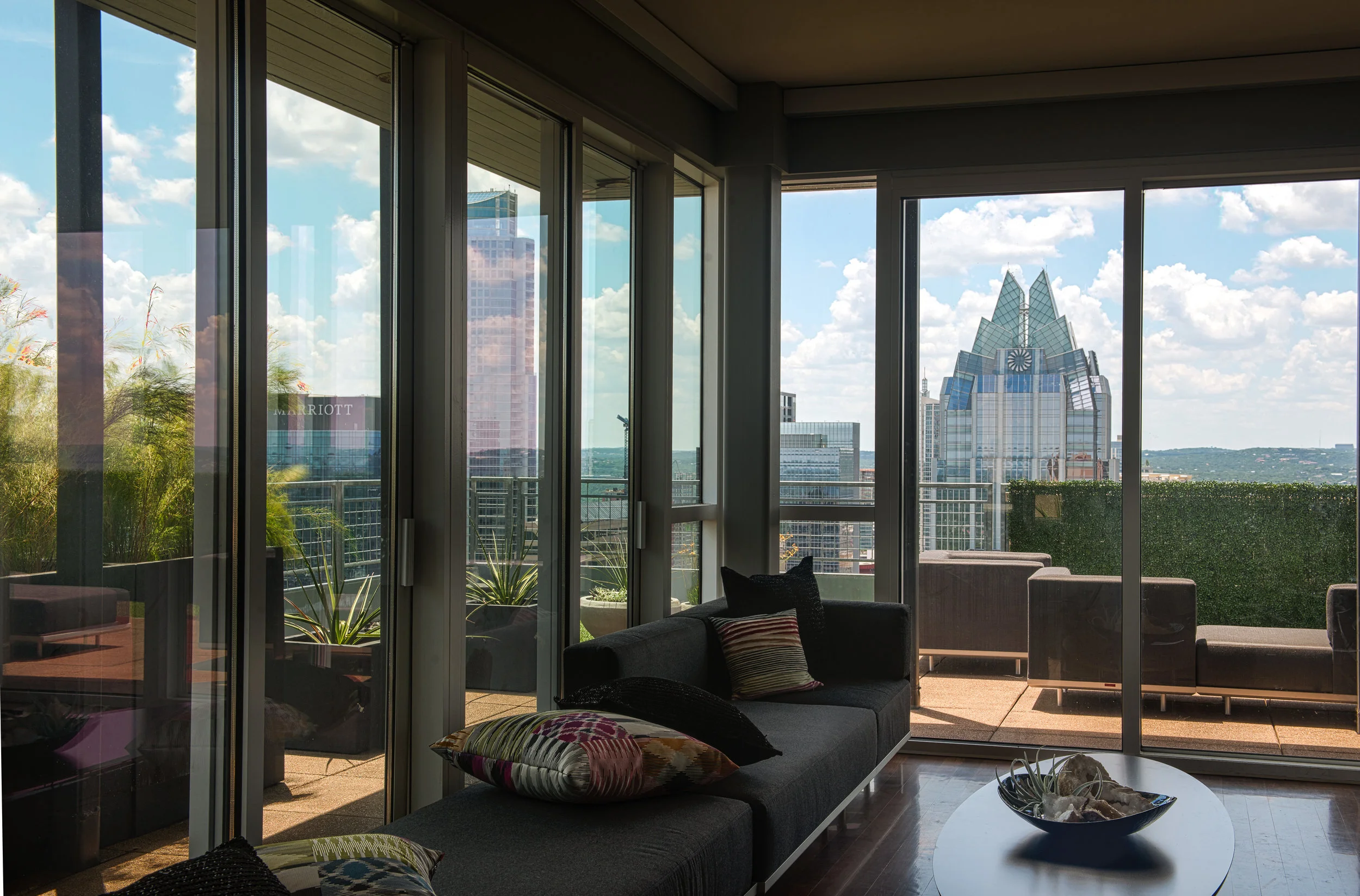 Living room in an Austin penthouse with a black sofa and large windows showcasing the city skyline and outdoor patio with seating.