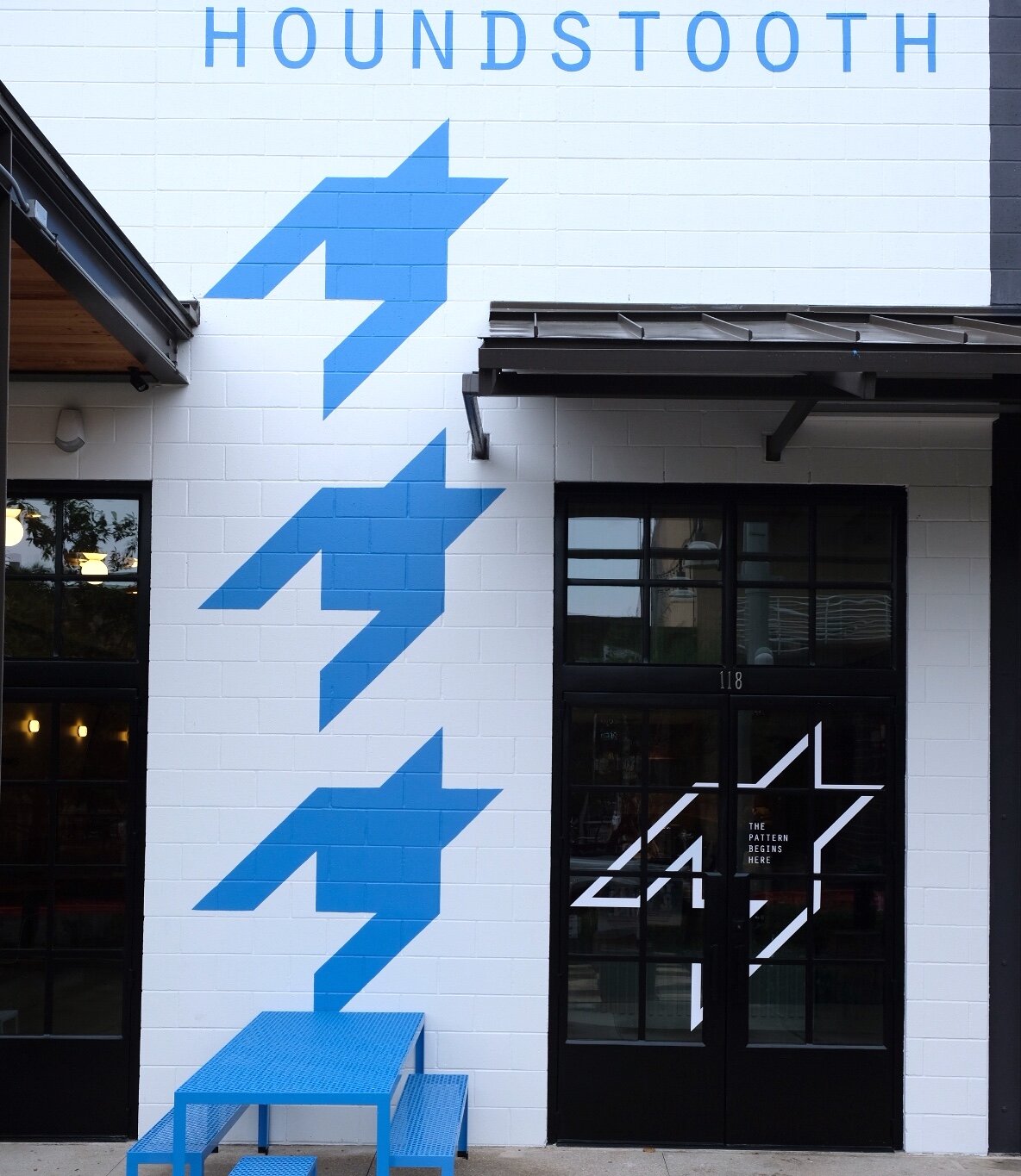 Exterior of Houndstooth Coffee NorthSide with a painted wall sign, blue geometric houndstooth pattern, and glass doors with a similar pattern.