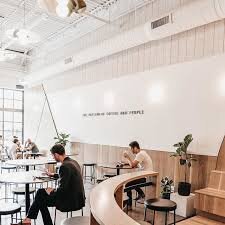 Houndstooth Coffee NorthSide spacious interior with customers seated at tables, a curved counter, large windows, and potted plants.