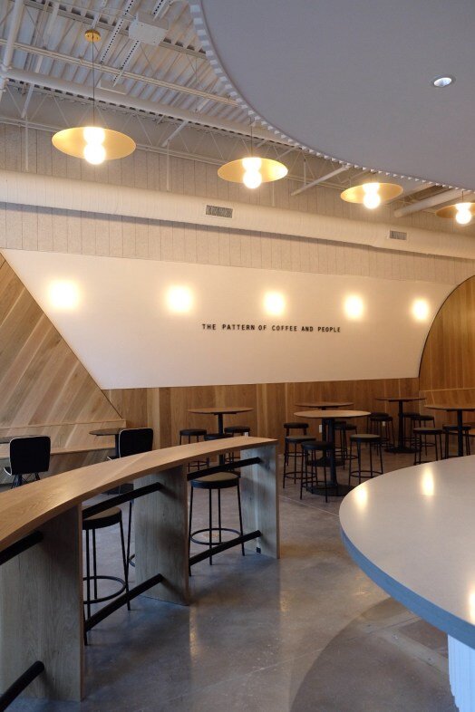 Interior of Houndstooth Coffee NorthSide with wooden tables, bar stools, and a wall sign reading "The Pattern of Coffee and People".