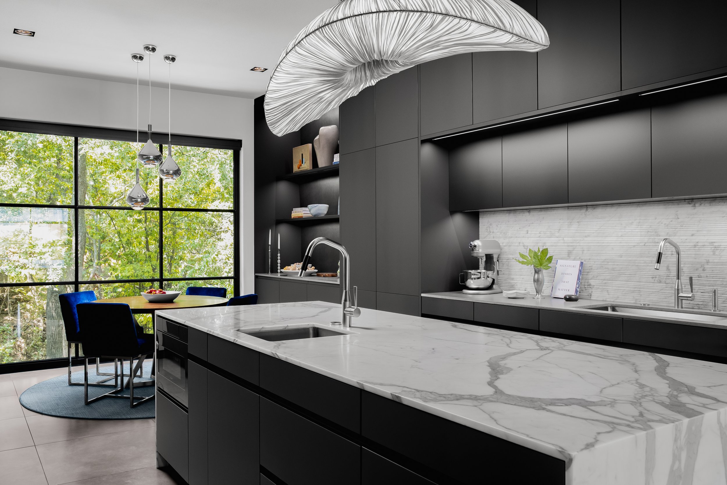 Kitchen in the Mediterranean Modern with black cabinets and marble countertops, featuring a large window, unique lighting, and dining area.