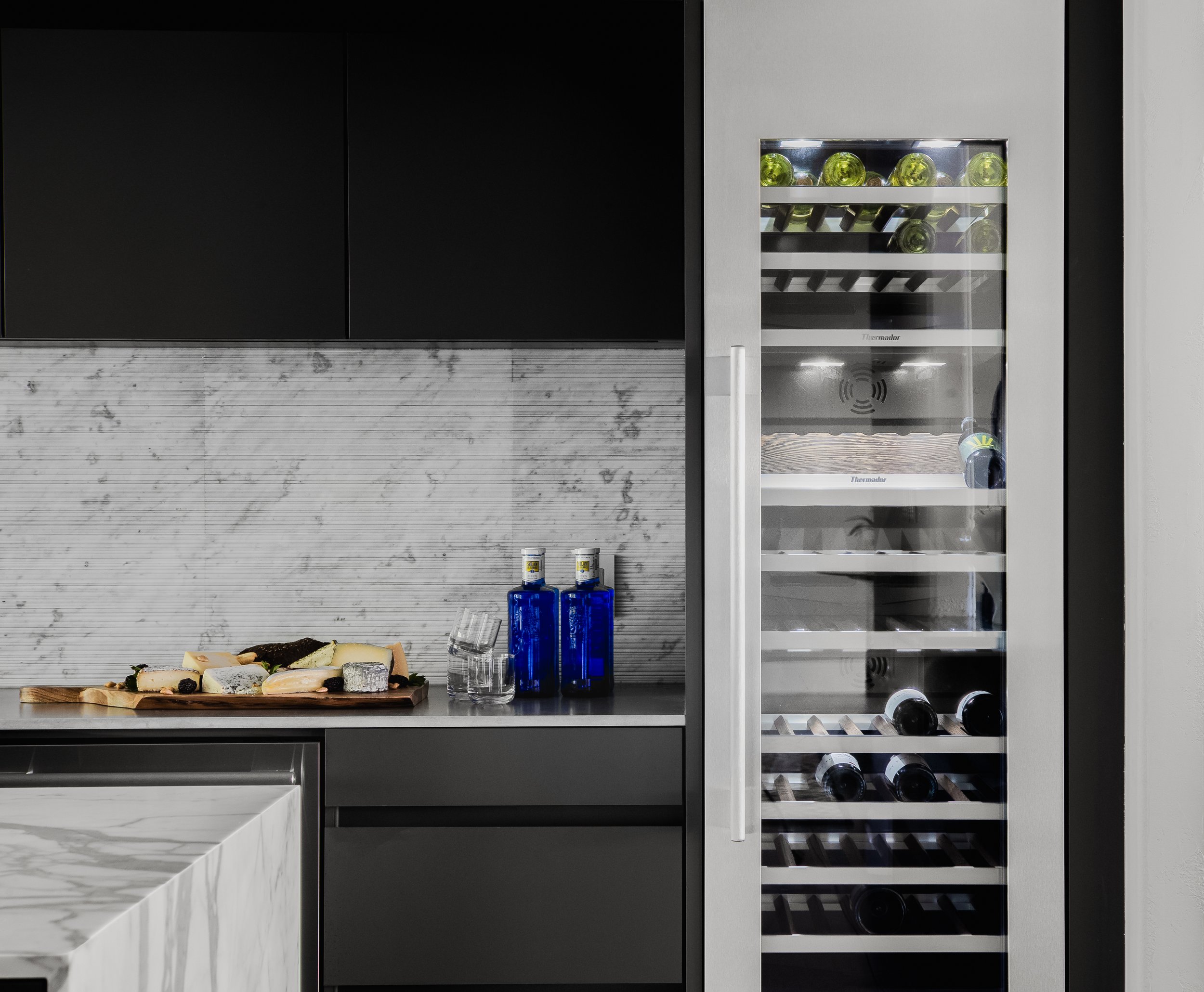 Kitchen in the Mediterranean Modern with a built-in wine cooler, marble countertop, cutting board, and blue water bottles.