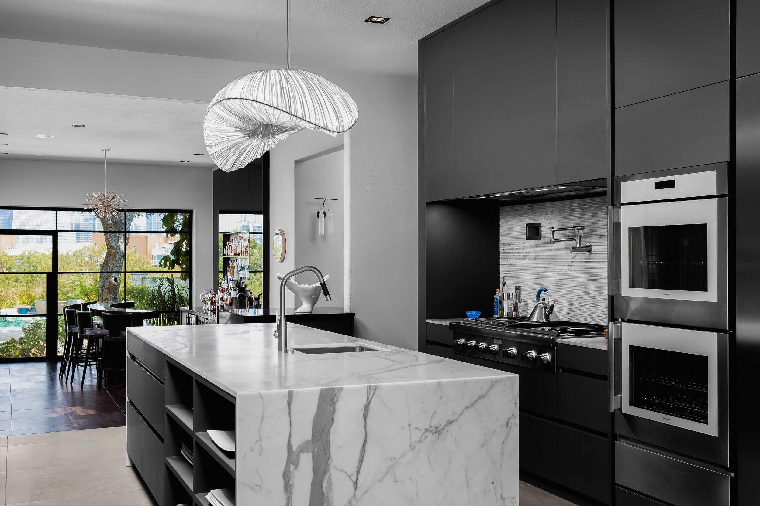 Black and white kitchen in the Mediterranean Modern with marble island, sleek cabinets, stainless steel appliances, and a large window view.