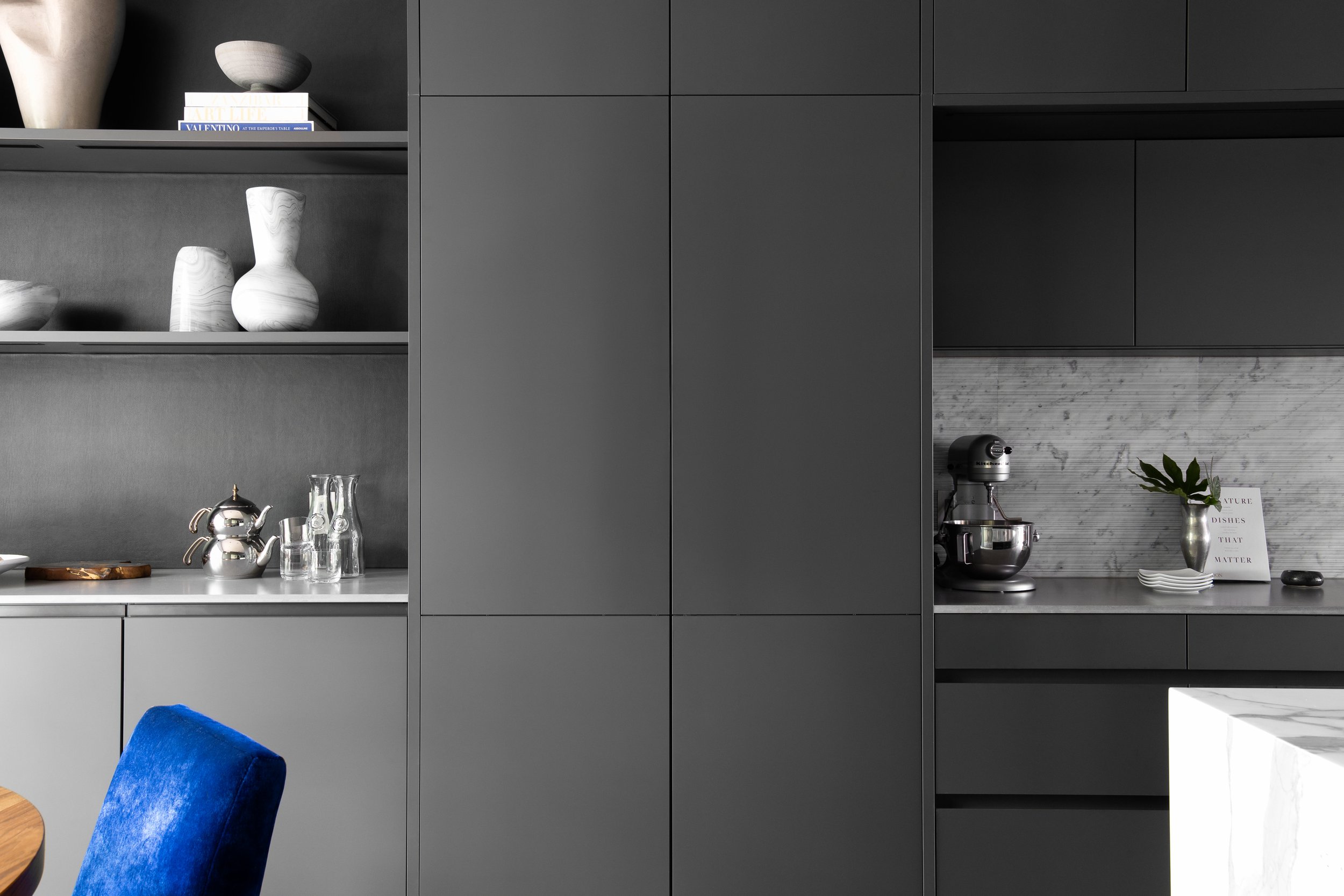 Kitchen in the Mediterranean Modern with dark gray cabinets, open shelves, white vases, books, silver kettle, glasses, and a stand mixer.