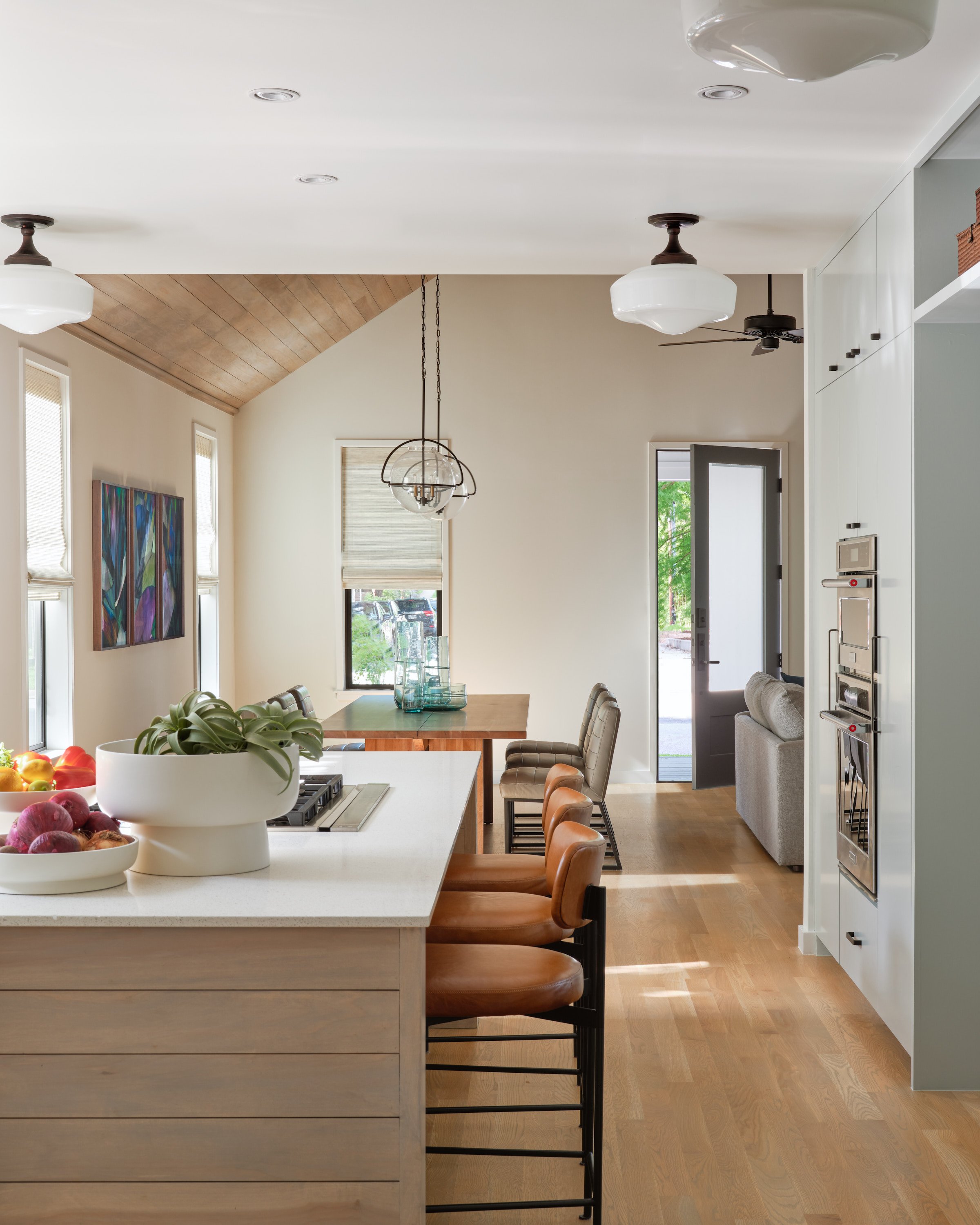 Kitchen in an East Side bungalow with a wooden island, leather barstools, pendant lights, and an open layout leading to a bright living area.