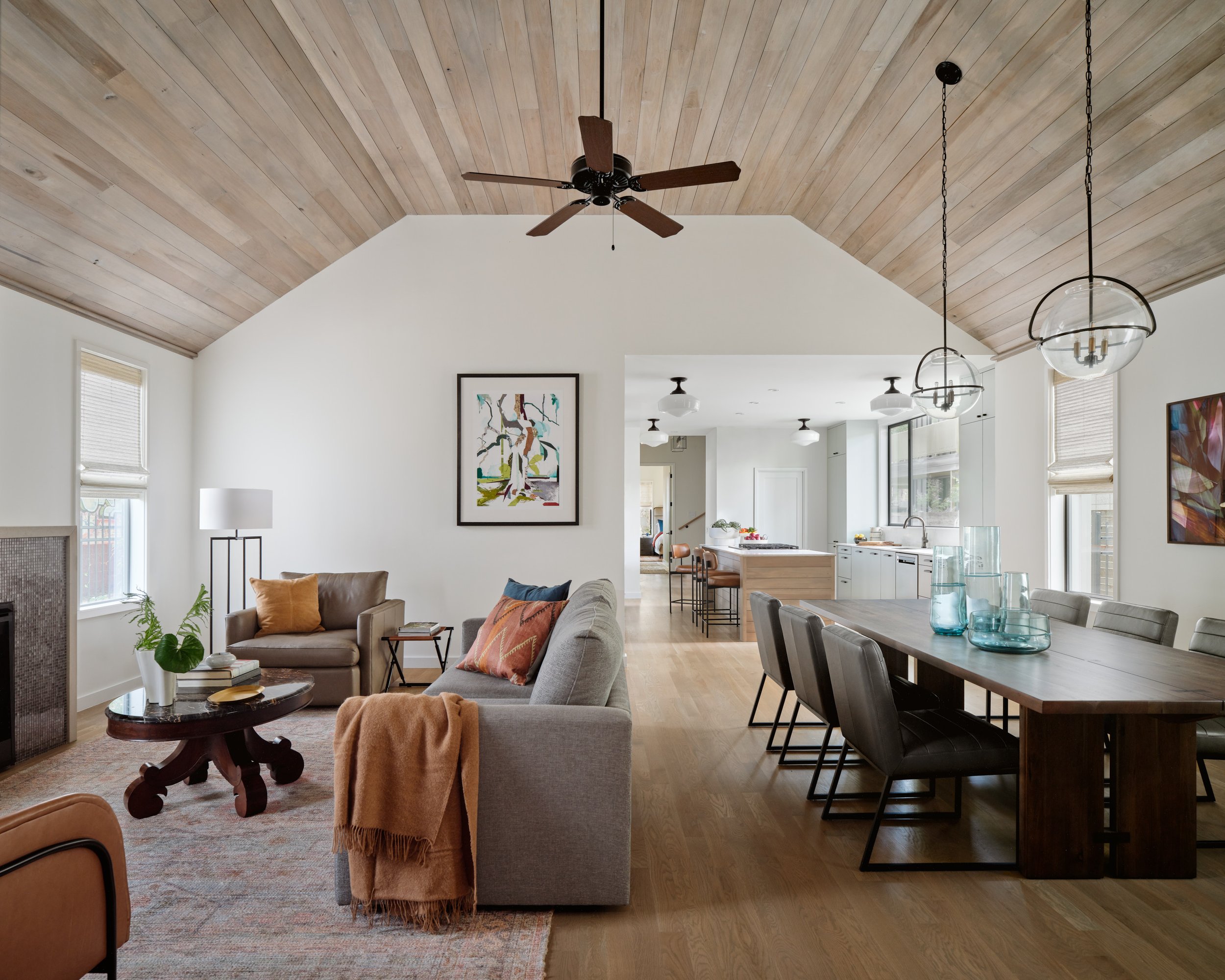 Open-concept living/dining area in an East Side bungalow with light wood ceiling, modern furnishings, art pieces, and a large dining table.