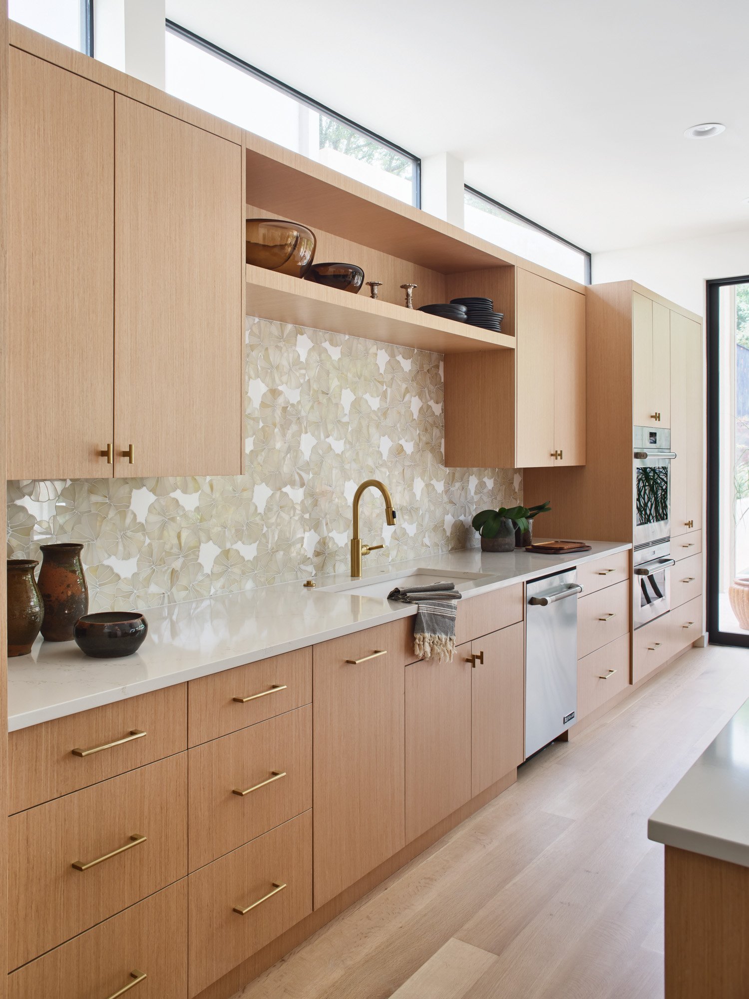 Kitchen in a Barton Creek home with light wood cabinets, decorative backsplash, golden fixtures, and stainless steel appliances.