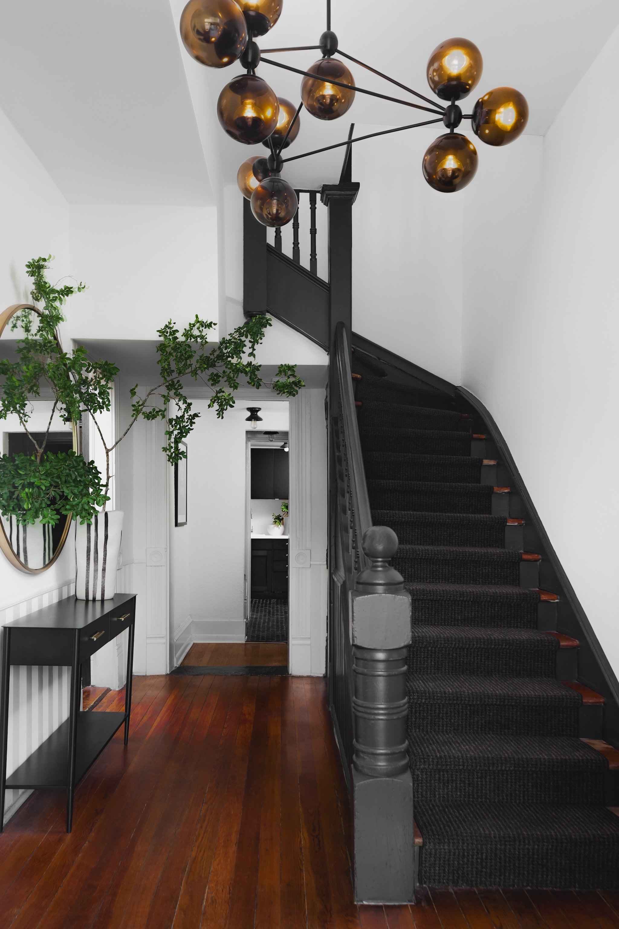 Staircase in a law firm with black railing and carpet, wooden flooring, round mirror, plants, and a black pendant light fixture.