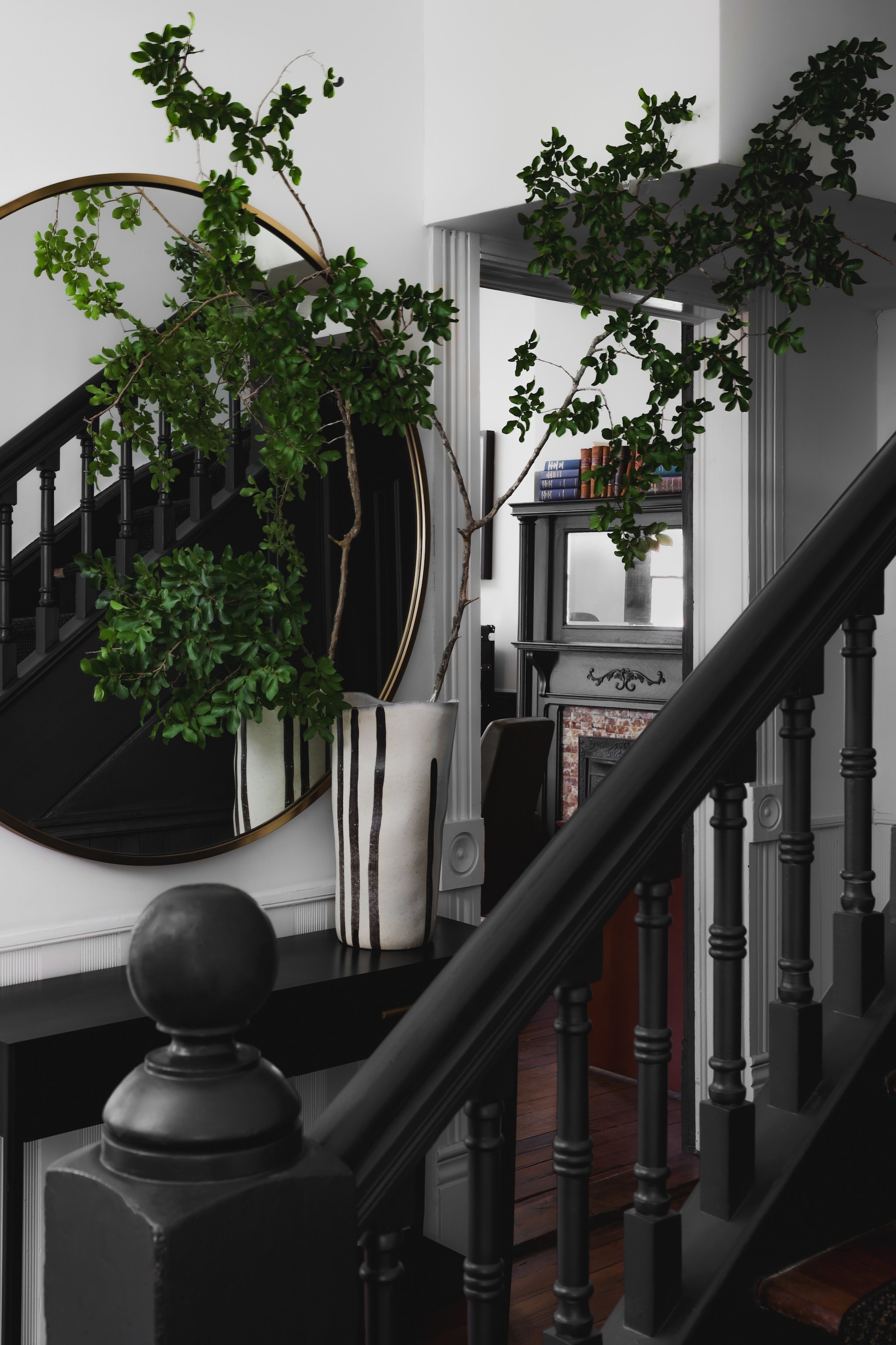 Staircase in a law firm with black railings, stylish large potted plant with green leaves, and a round mirror.