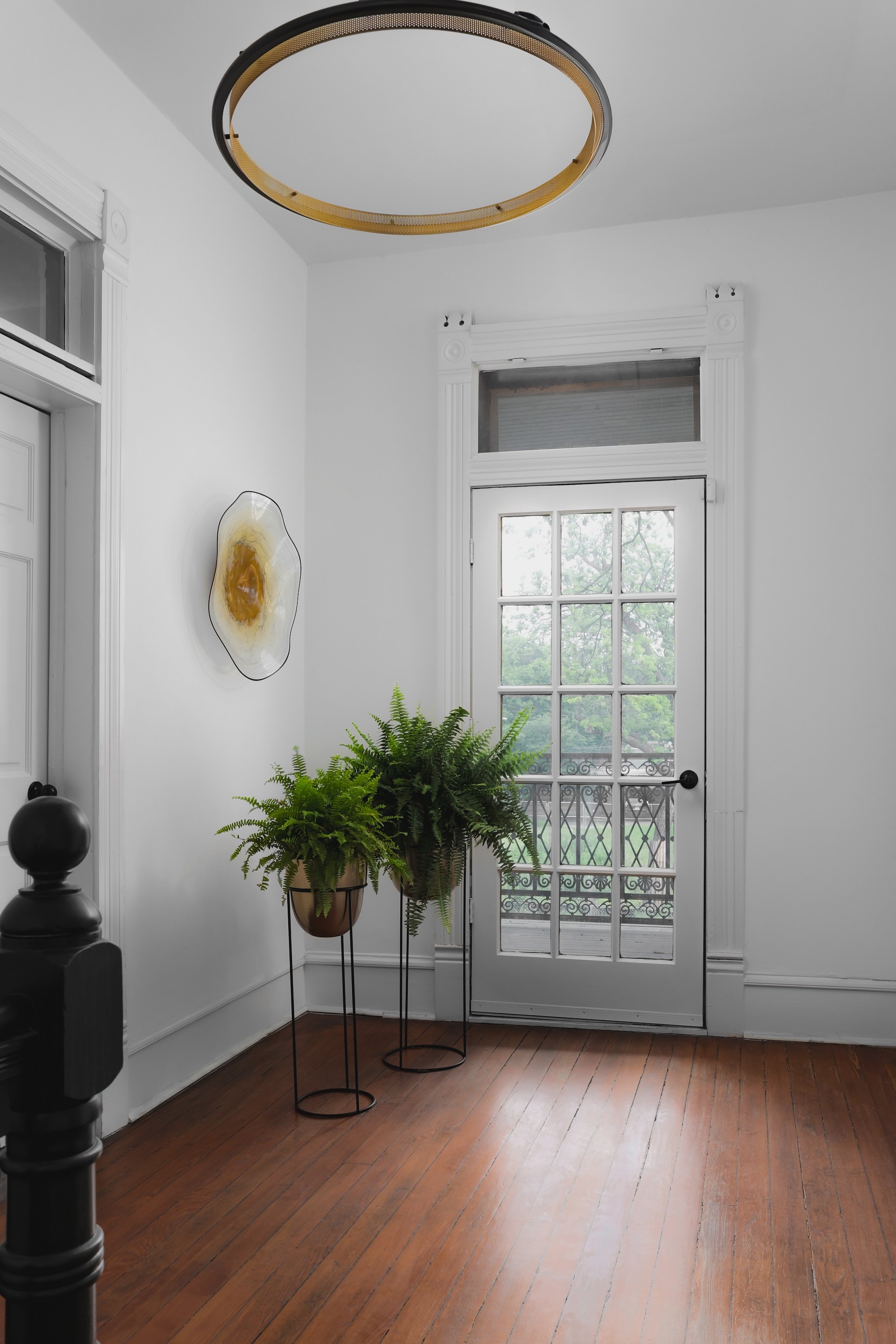 Minimalist room in a law firm with a wooden floor, two potted ferns on stands, large circular light fixture, and a door leading outside.