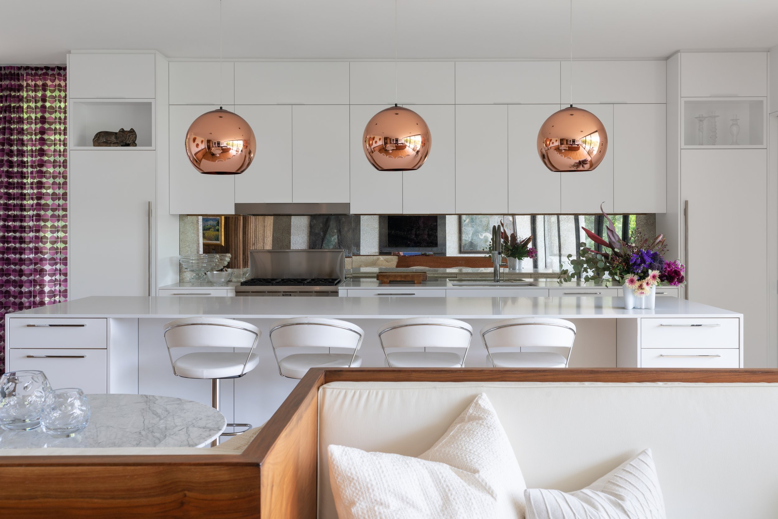 Kitchen in a Laurel Canyon home with white cabinetry, a large island with four stools, and three copper pendant lights hanging overhead.