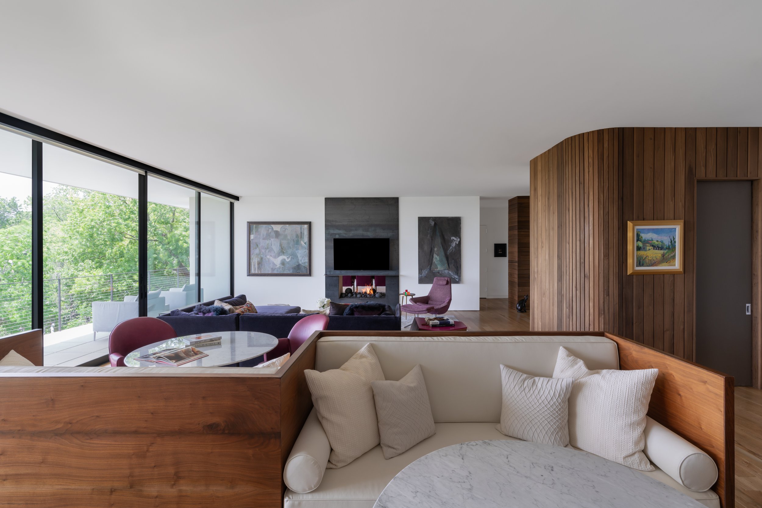 Open-plan living room in a Laurel Canyon home with large windows, modern furniture, a small round table, and a TV mounted above a fireplace.