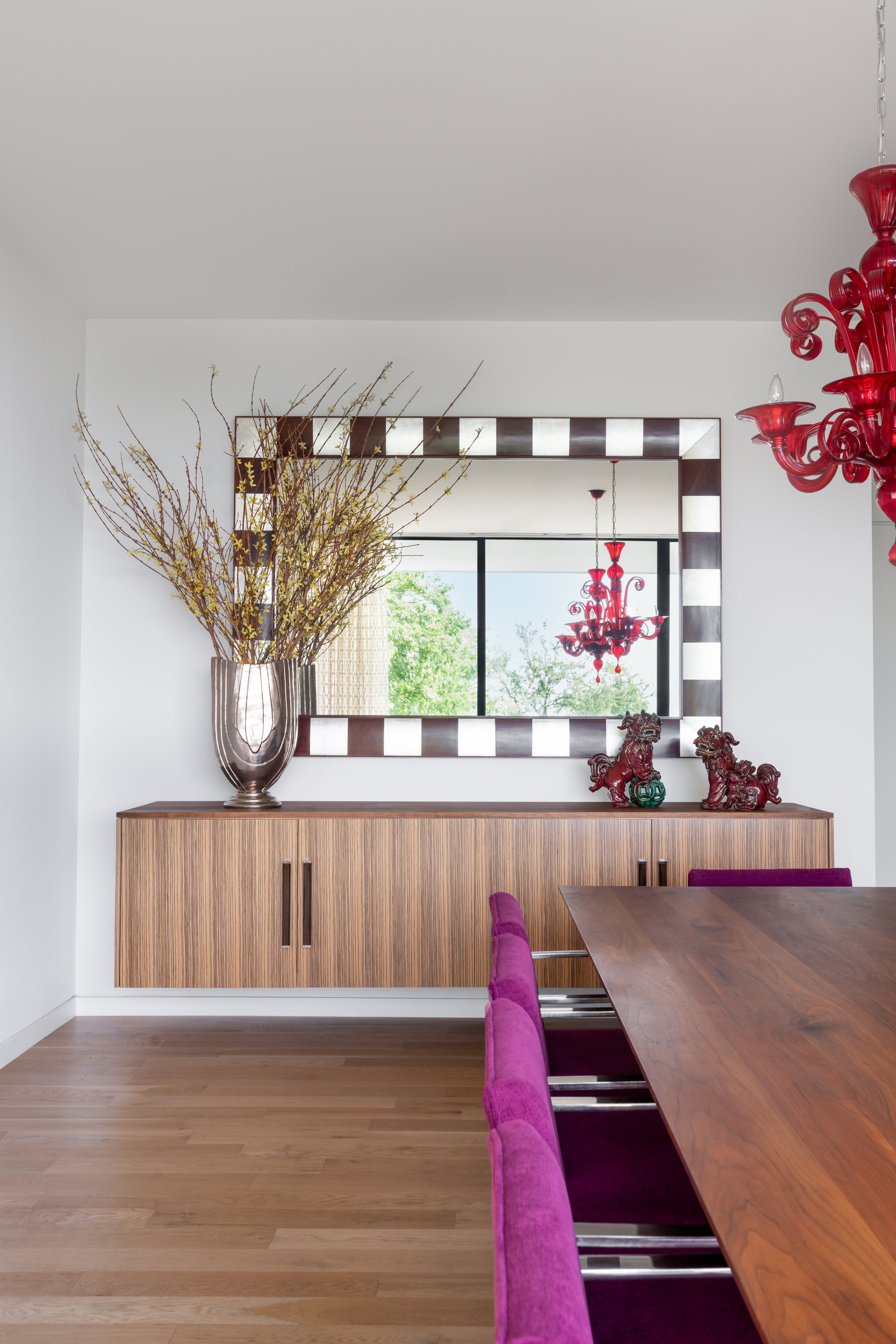 Dining room in a Laurel Canyon home with a wooden table, purple fabric chairs, a checkered mirror, and red chandelier.