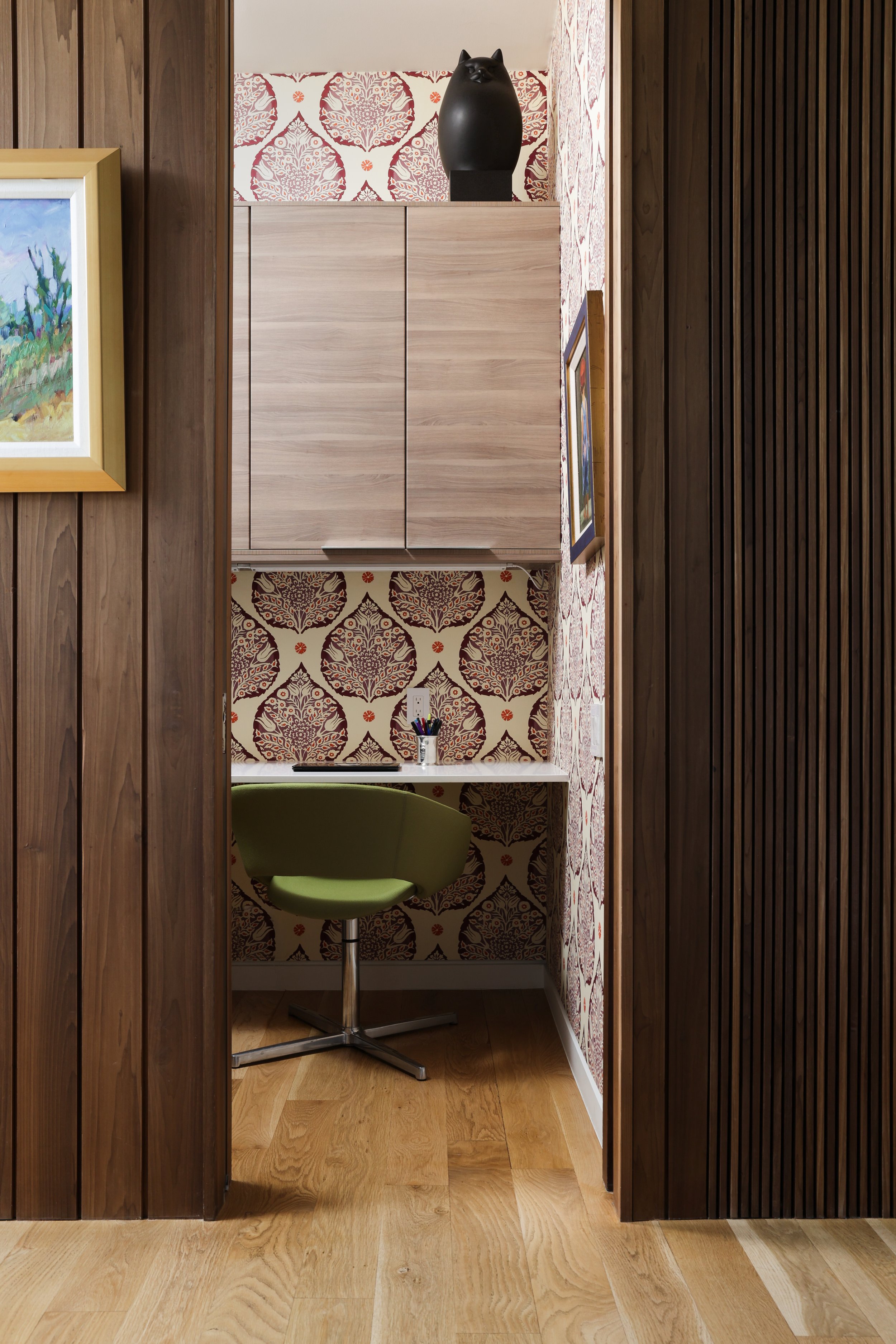 Compact workspace in a Laurel Canyon home with a green chair, wall mounted cabinets, decorative wallpaper, and wooden paneling on the sides.