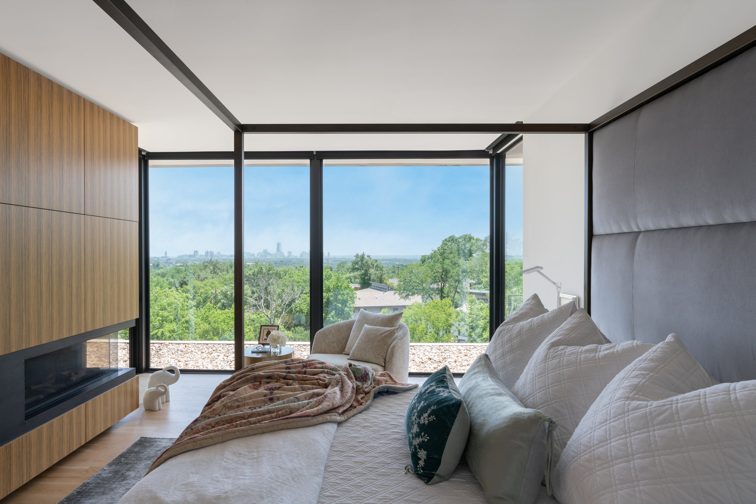 Bedroom in a Laurel Canyon home with a large bed, light wood accents, and floor-to-ceiling windows revealing greenery and the Los Angeles cityscape outside.