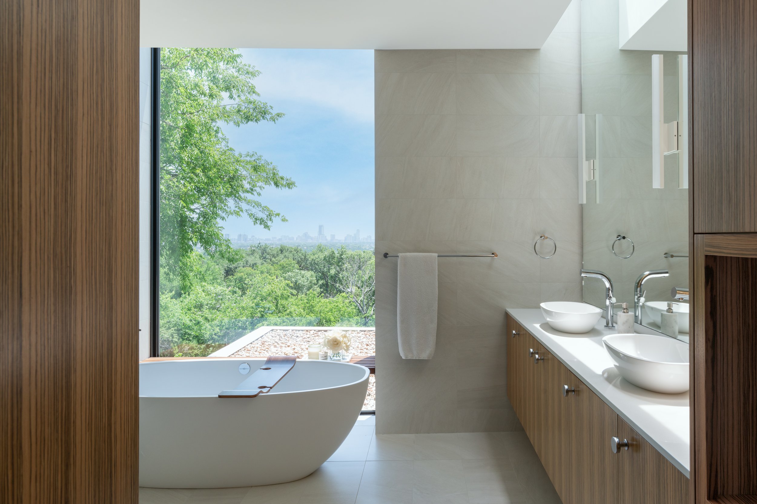 Bathroom in a Laurel Canyon home with large window showcasing a lush green view, freestanding bathtub, and double sinks on a wooden vanity.
