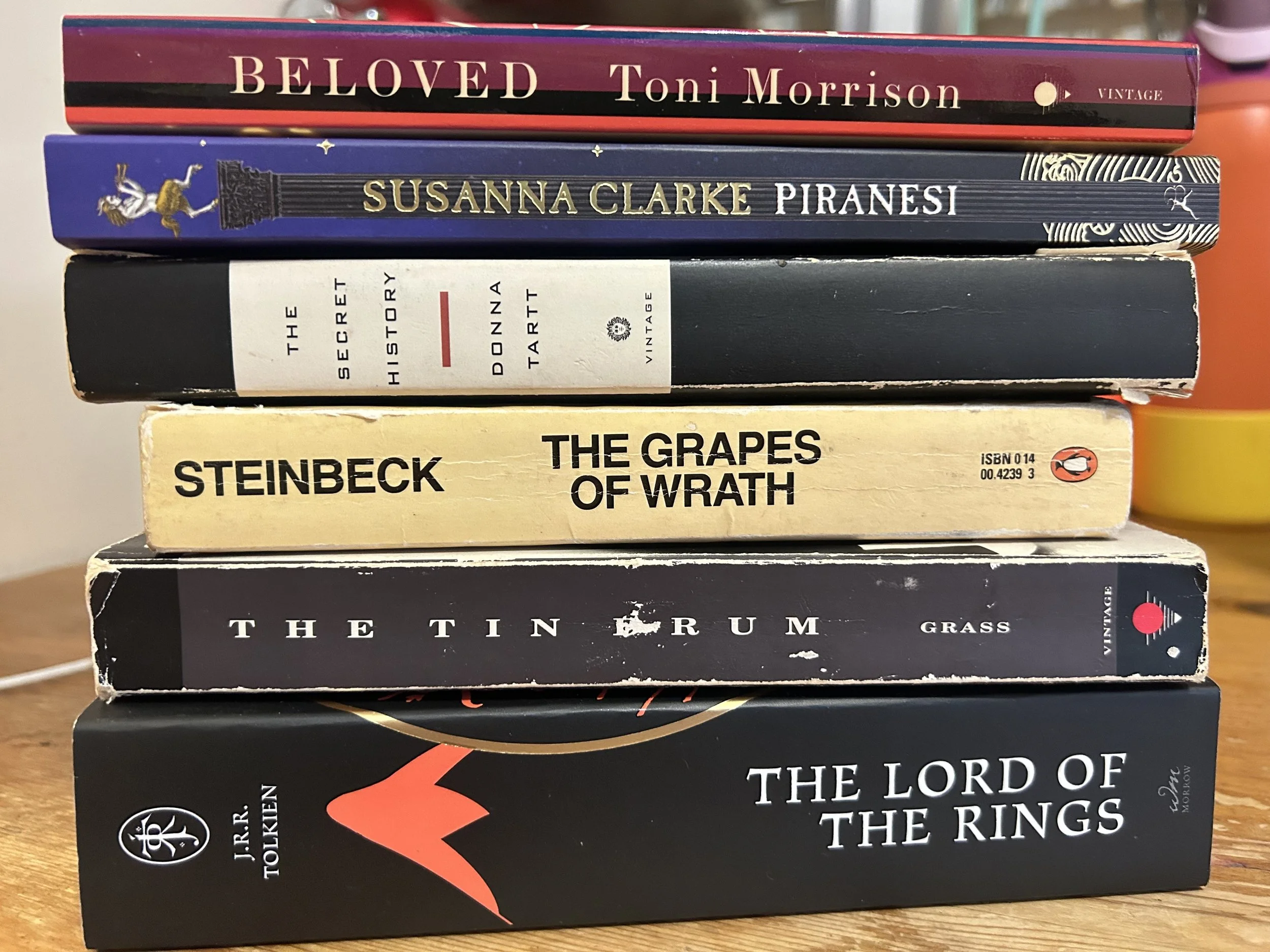 A stack of books, including Beloved, Piranesi, The Secret History, The Grapes of Wrath, The Tin Drum, and The Lord of the Rings