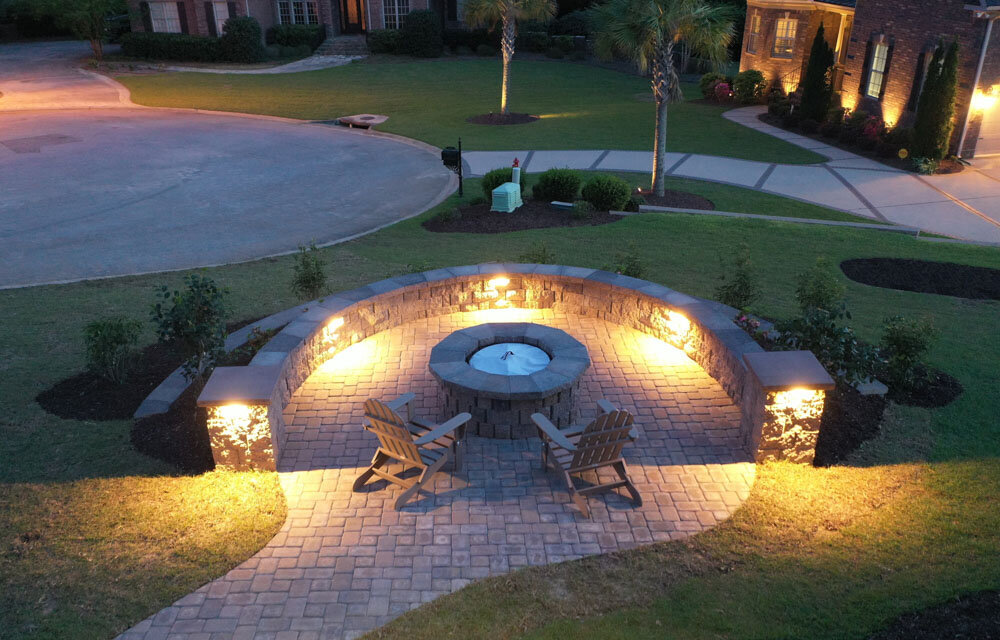 Elegant Outdoor Decor, Lighting, and Fire Pit with Seat Wall by Saluda Hill Landscapes