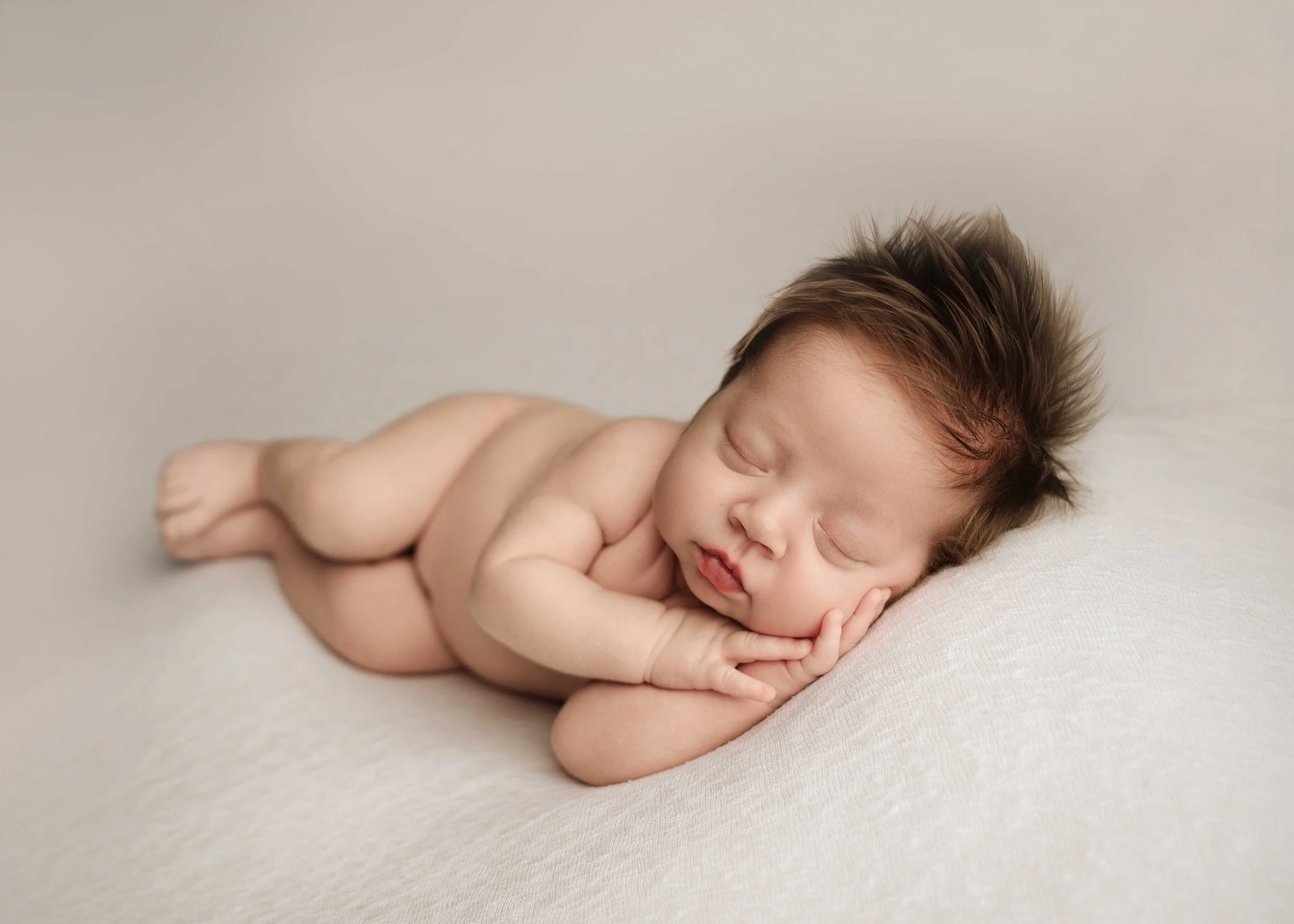 baby boy with lots of hair lays on cream blanket in a side-lying pose