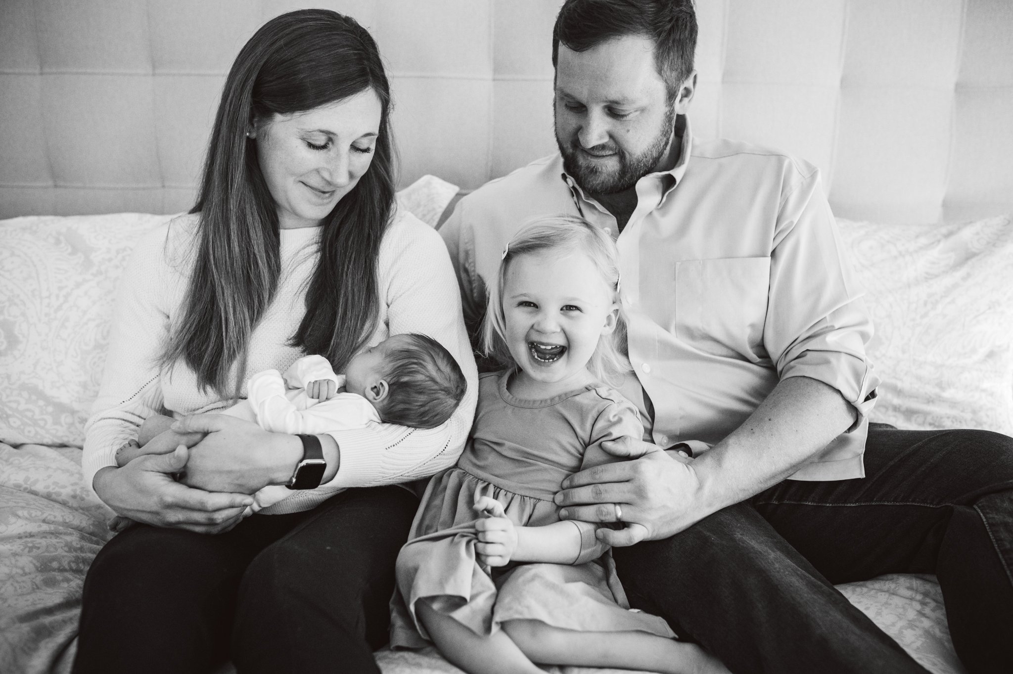 Family of four on bed, toddler laughing